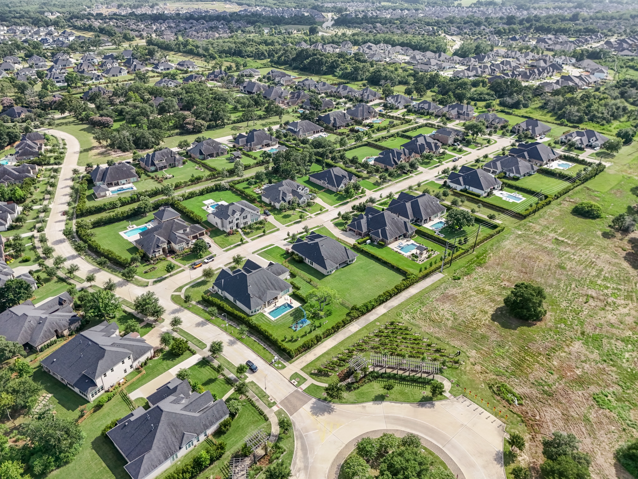 A sprawling residential development nestled among lush greenery, with neatly arranged houses, roads, and landscaped yards visible from an aerial perspective.