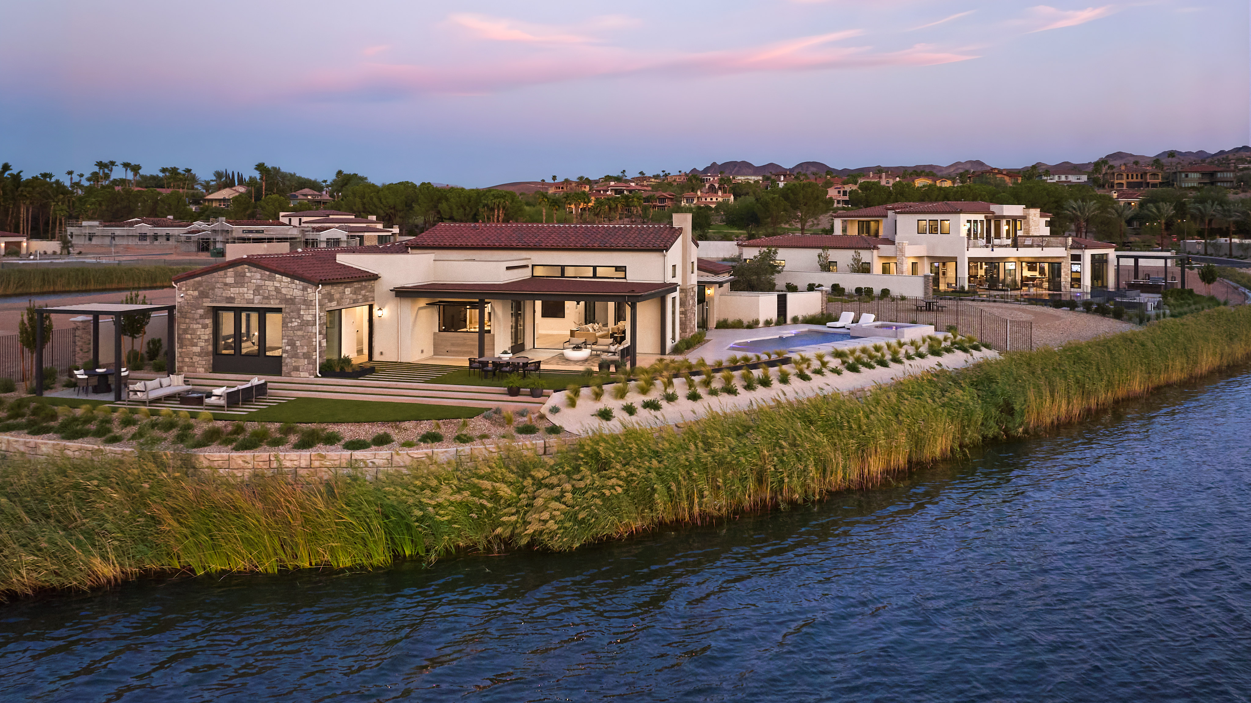 A scenic waterfront community with modern homes and buildings nestled among lush greenery, set against a vibrant sunset sky.