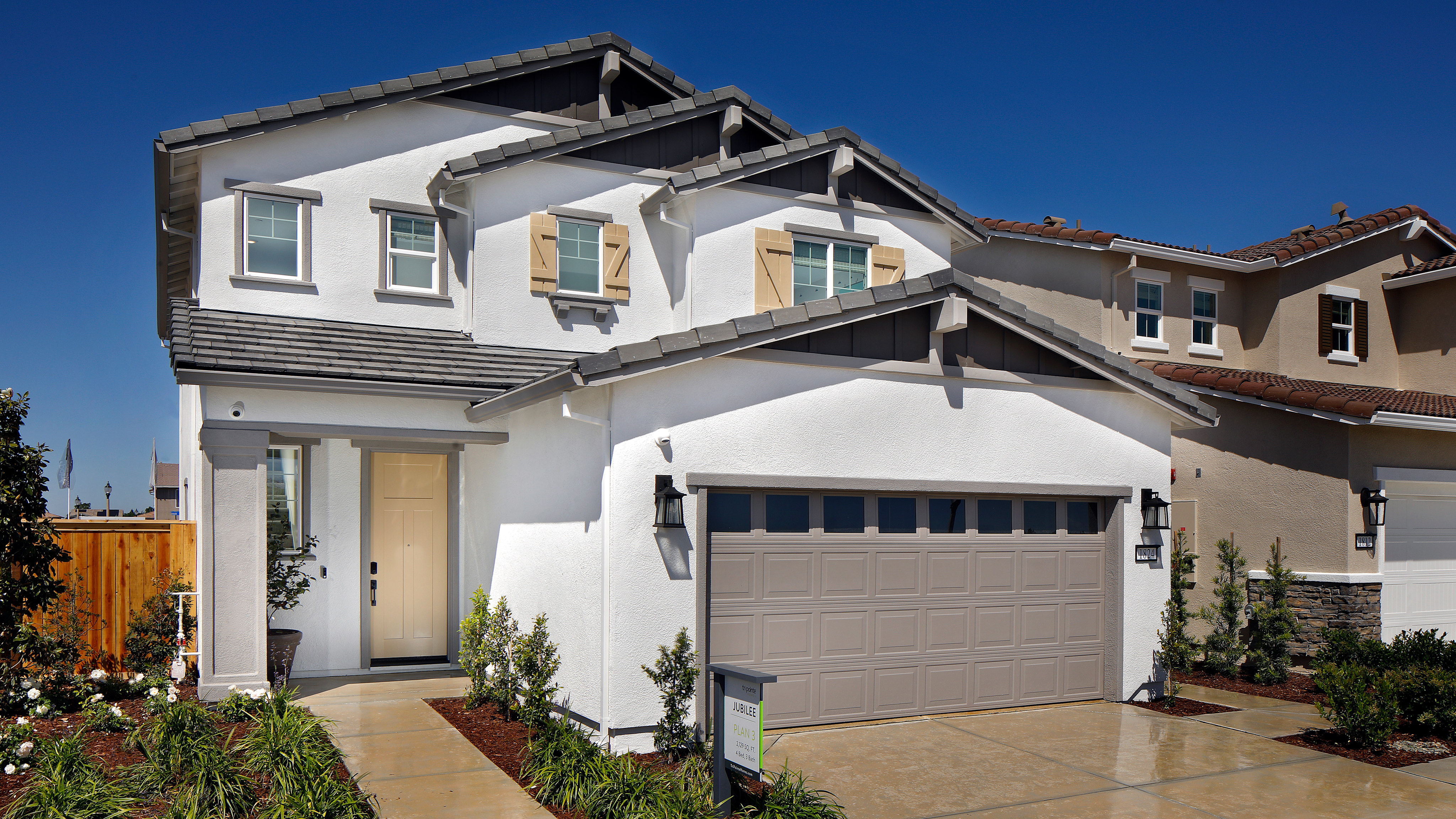 A two-story residential house with a garage, surrounded by a well-maintained lawn and landscaping, set against a clear blue sky.