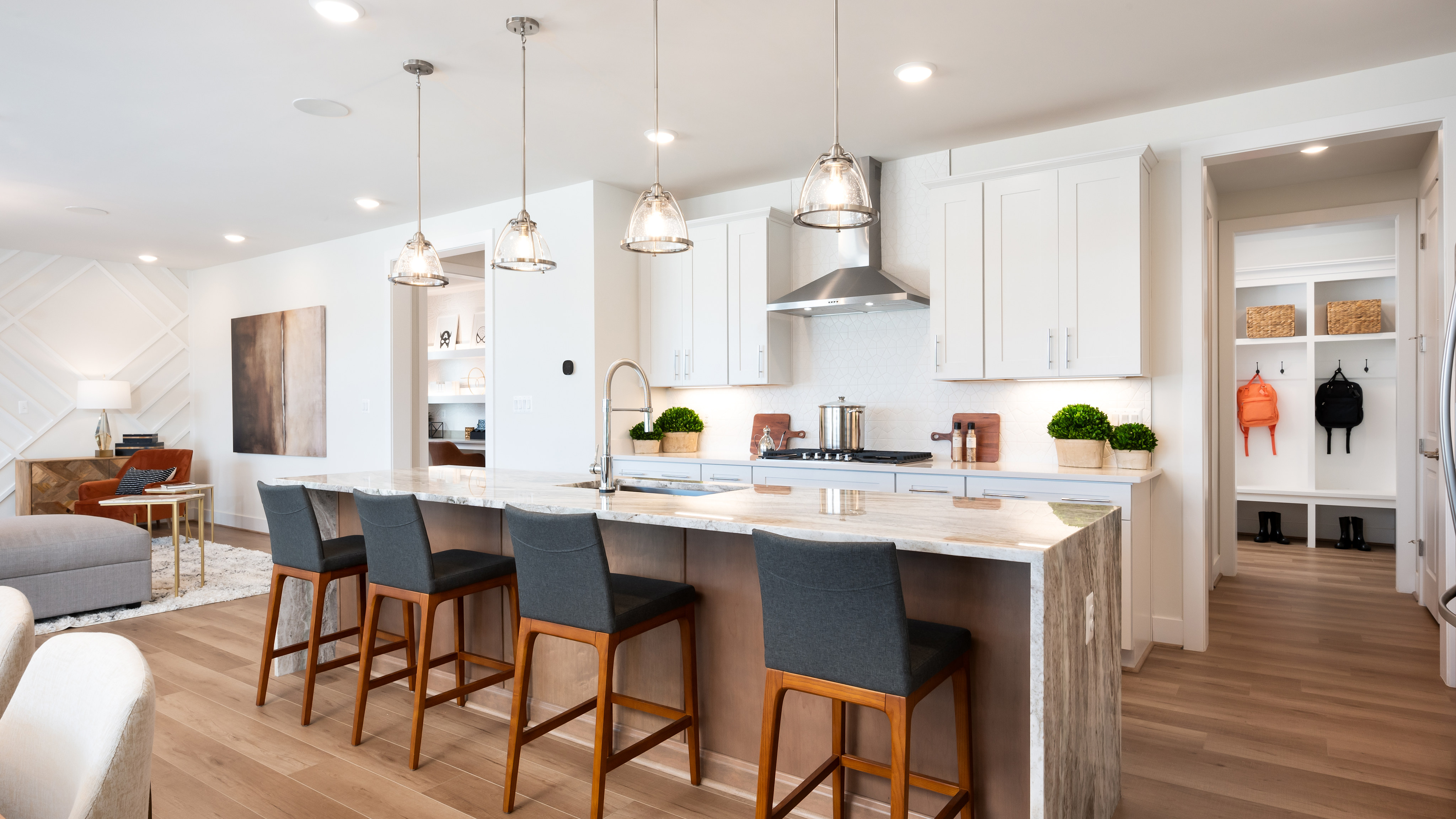 A modern, open-concept kitchen with white cabinets, wooden countertops, and pendant lights hanging above a central island with bar stools.