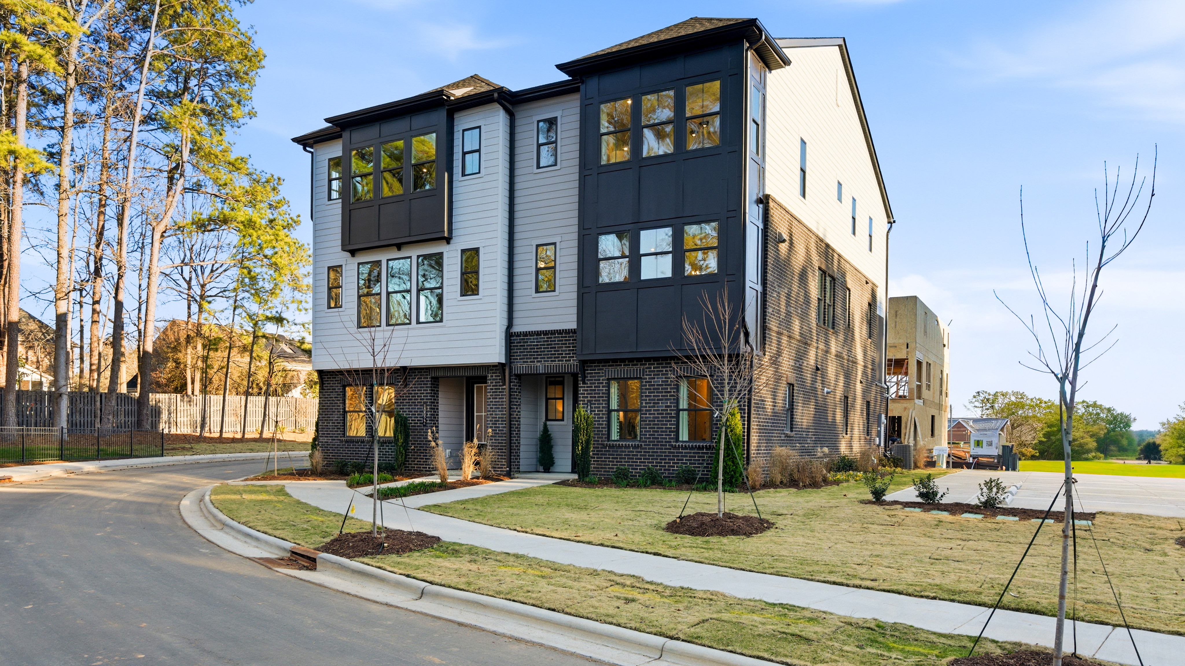 A modern multi-story residential building with a mix of siding materials, surrounded by a well-landscaped yard and trees in the background.