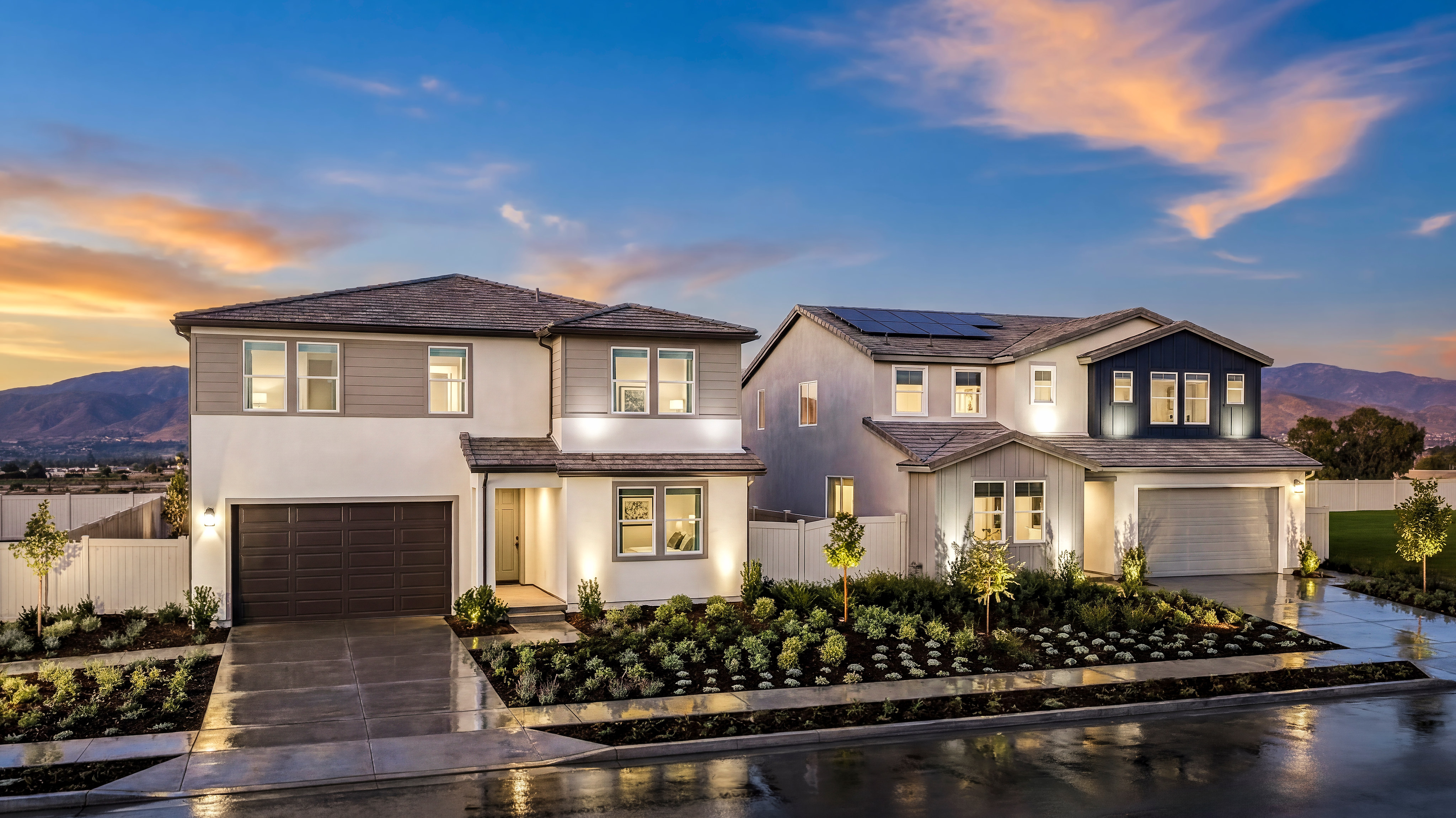A modern, multi-story residential home with a well-landscaped front yard sits against a backdrop of a vibrant sunset sky.