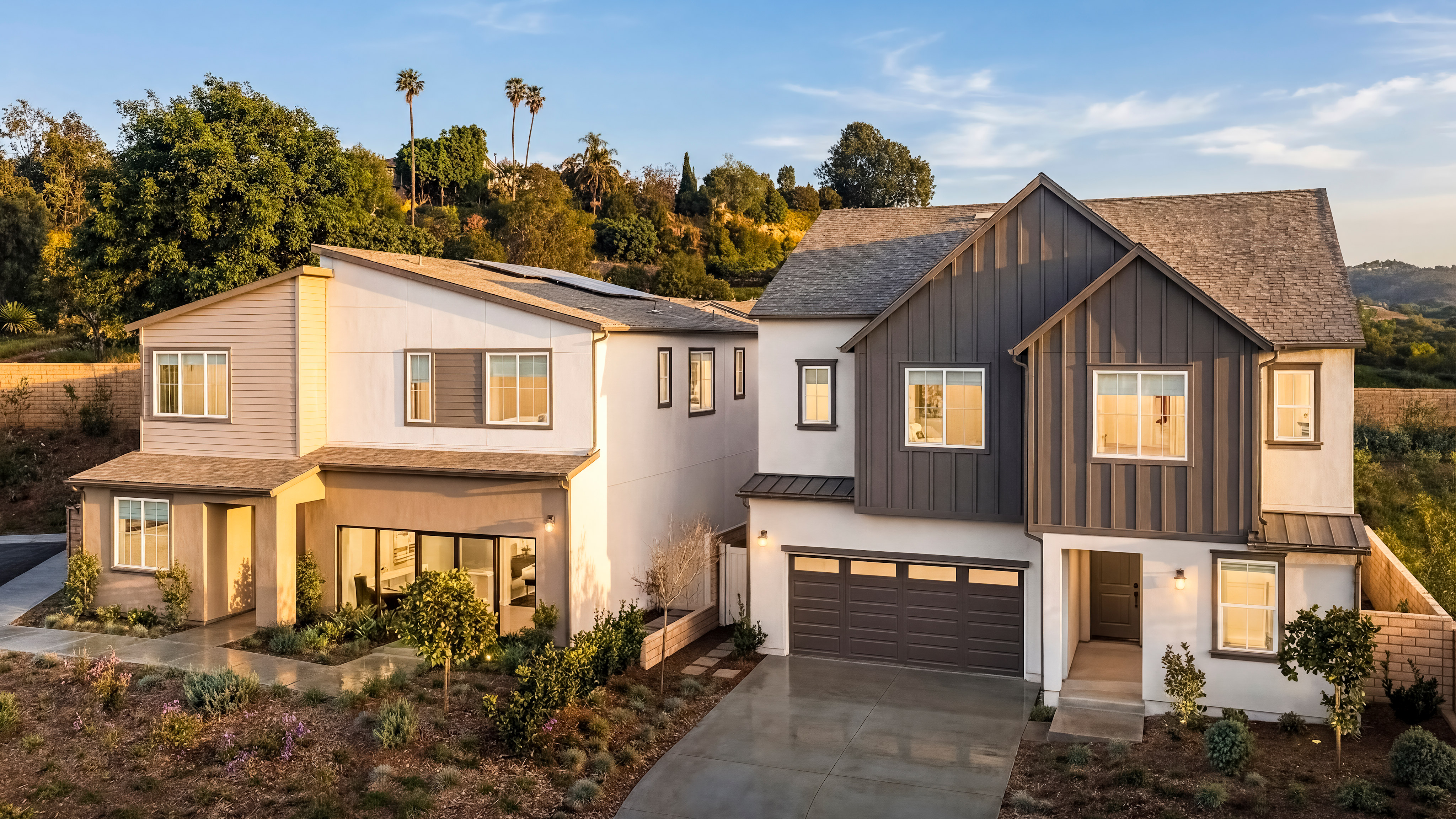 A two-story residential house with a garage, surrounded by trees and a hilly landscape in the background, bathed in warm evening light.