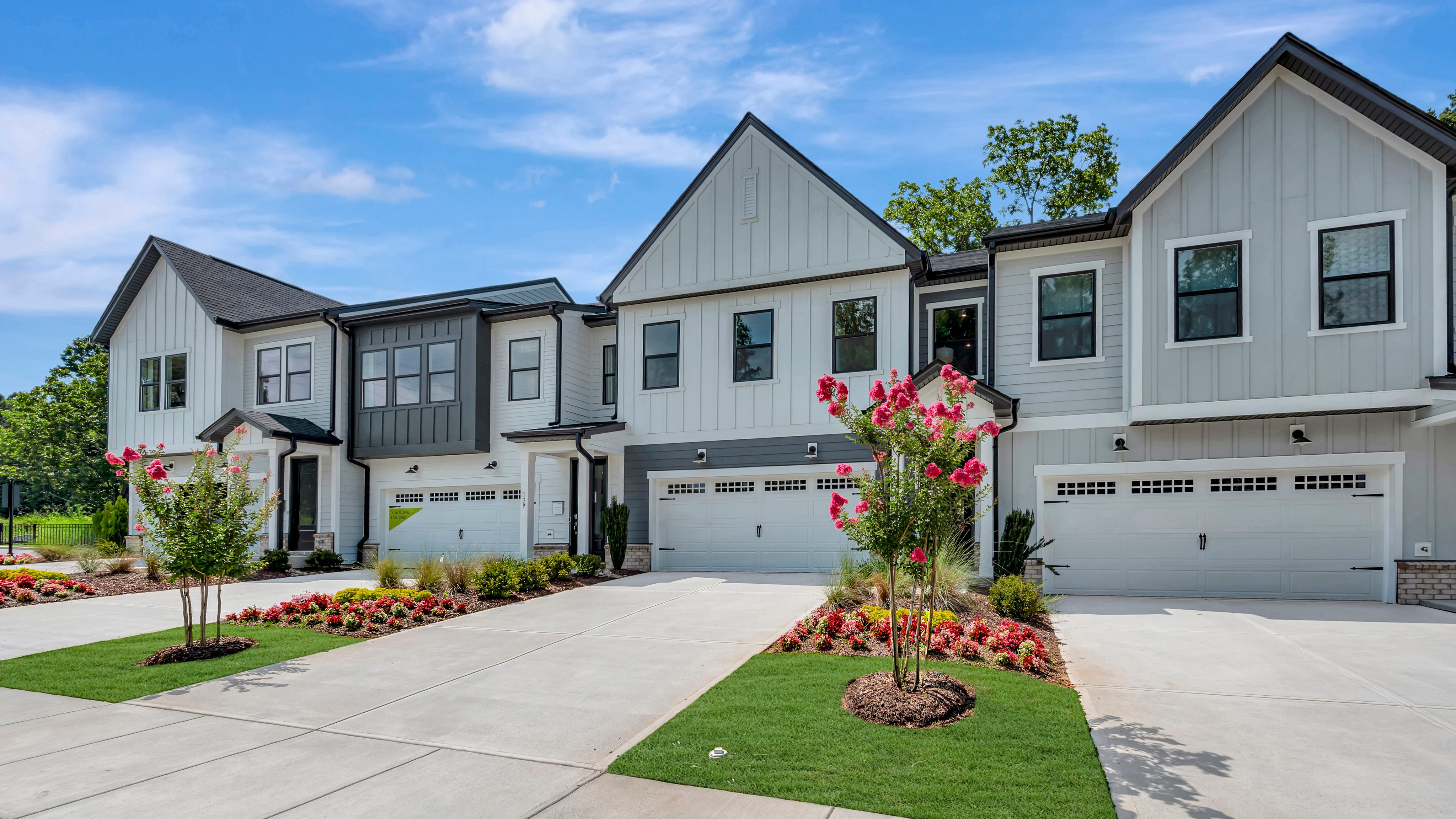 Modern townhouses with manicured landscaping in the foreground stand against a bright blue sky with fluffy clouds.