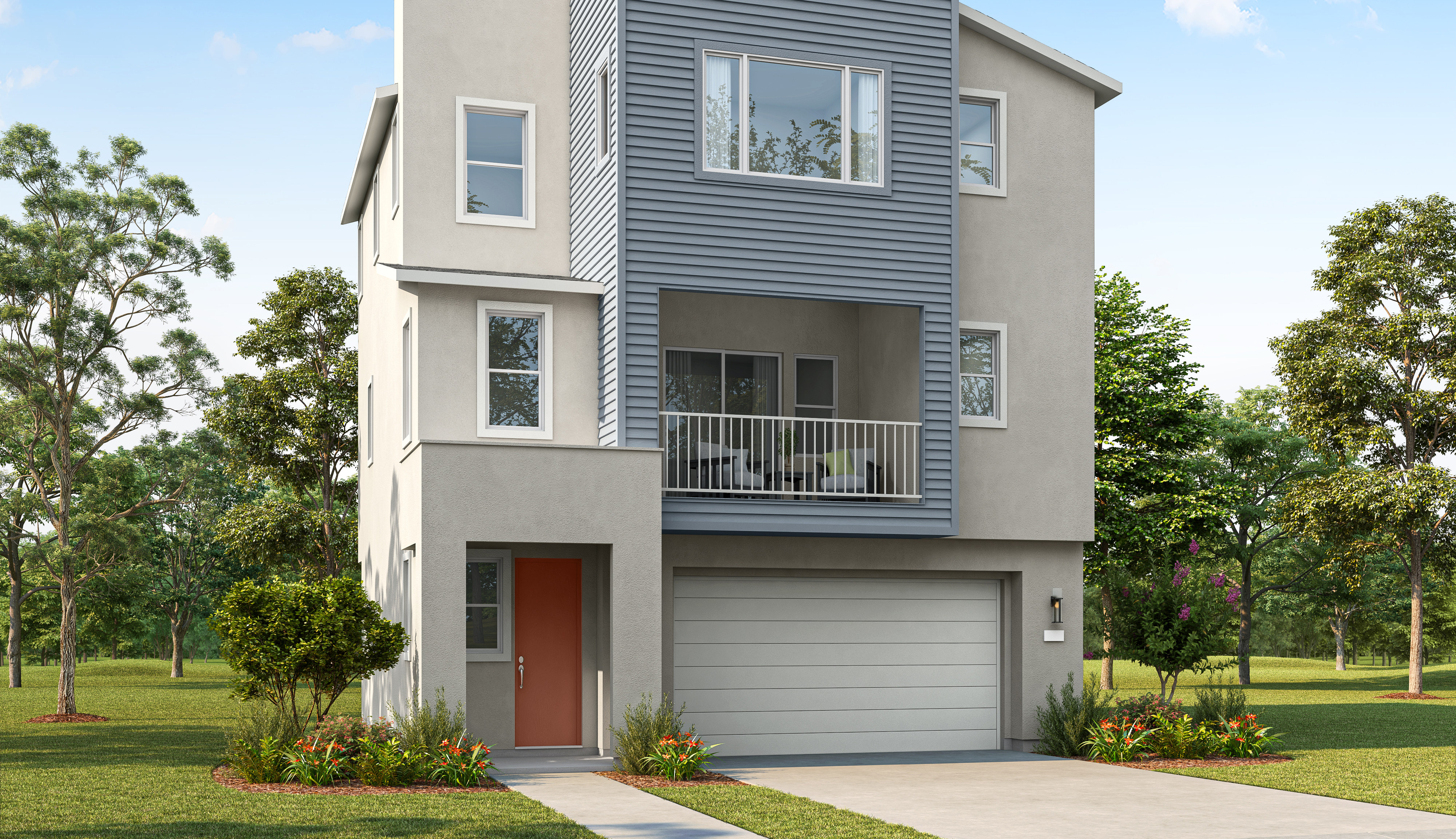 A modern, multi-story house with a gray and beige exterior and a balcony sits in front of a backdrop of lush green trees and a clear blue sky.