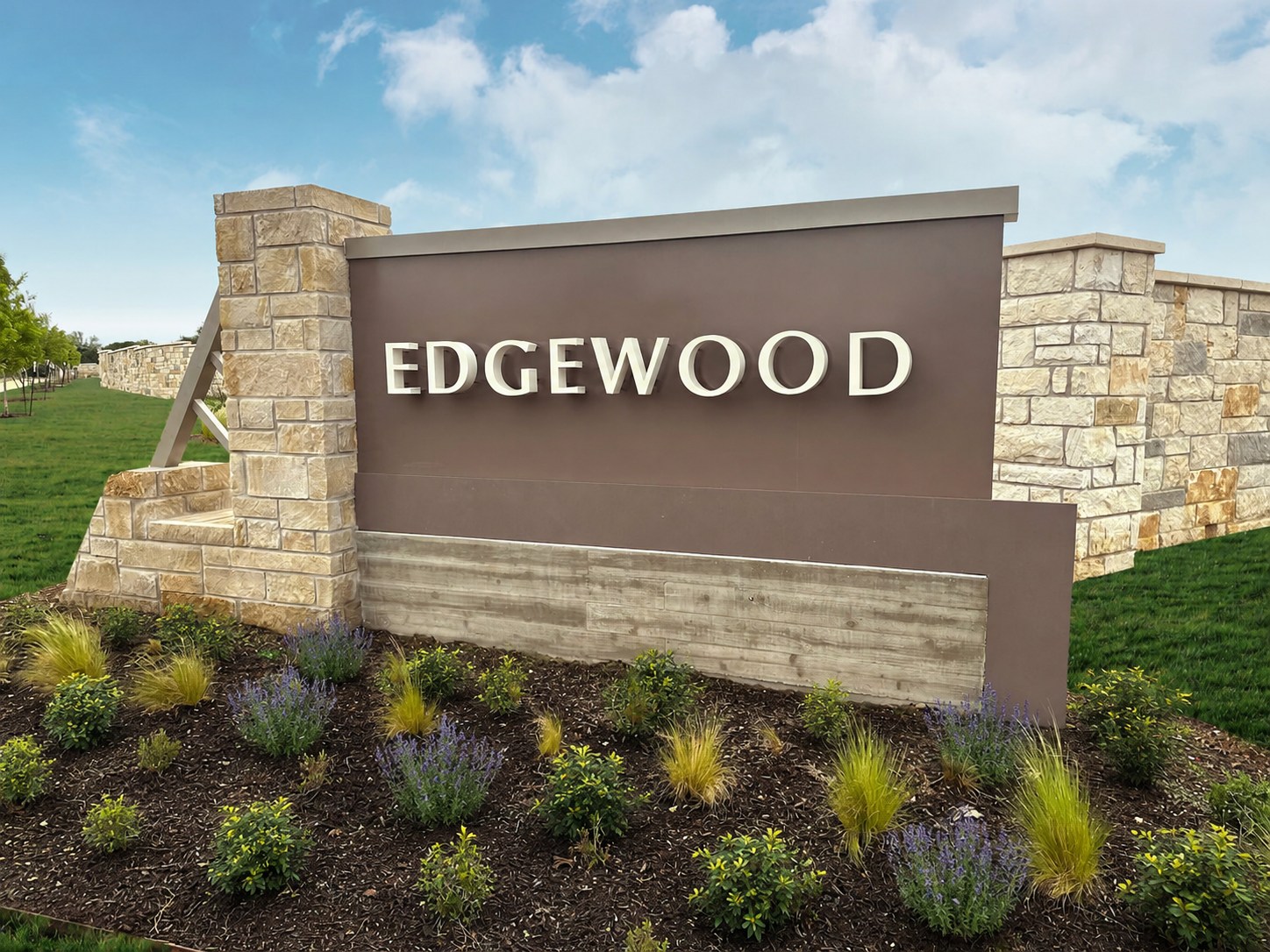 A large "EDGEWOOD" sign with stone pillars stands in front of a grassy area with a cloudy sky.