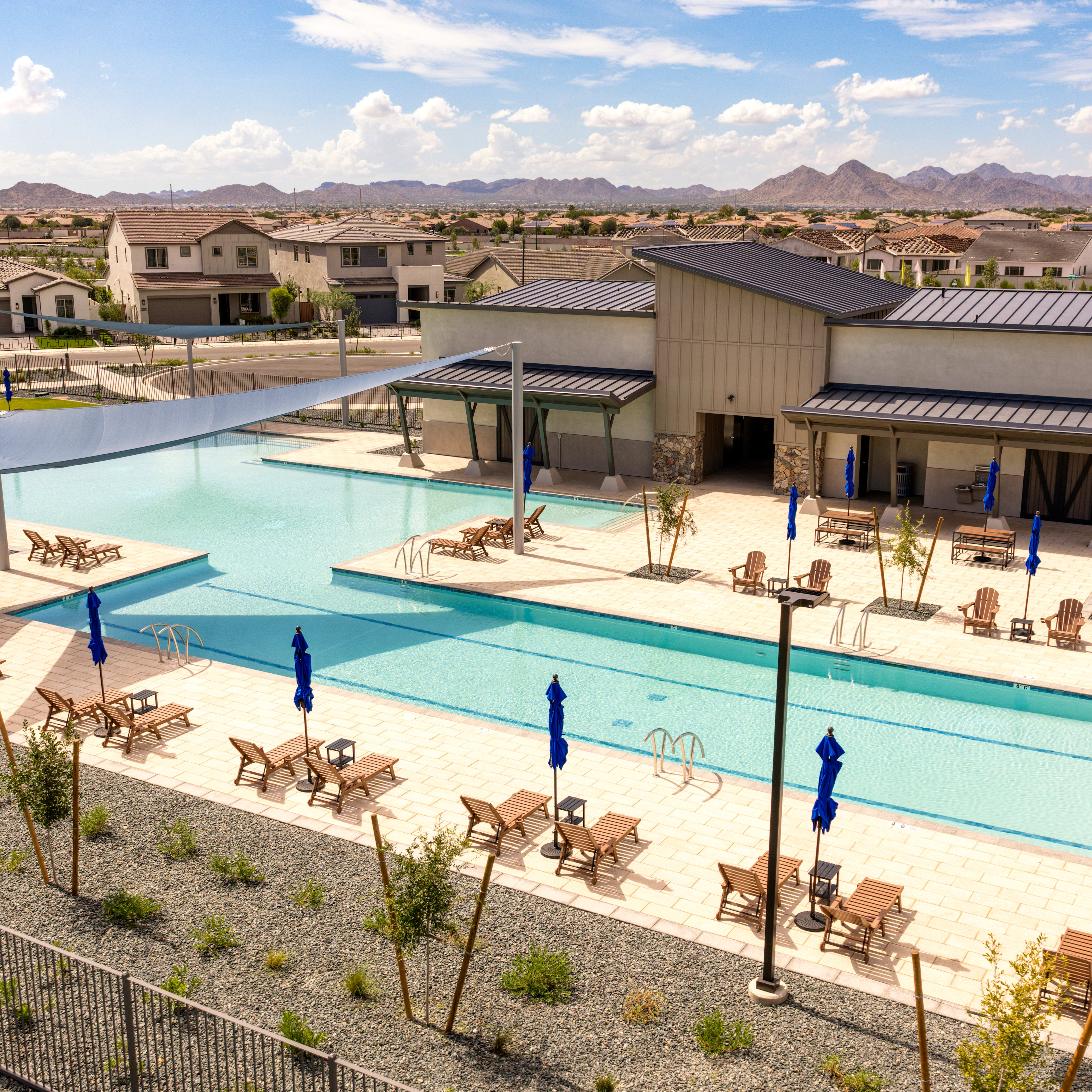 A residential community with a large swimming pool surrounded by buildings, chairs, and a mountainous landscape in the background.