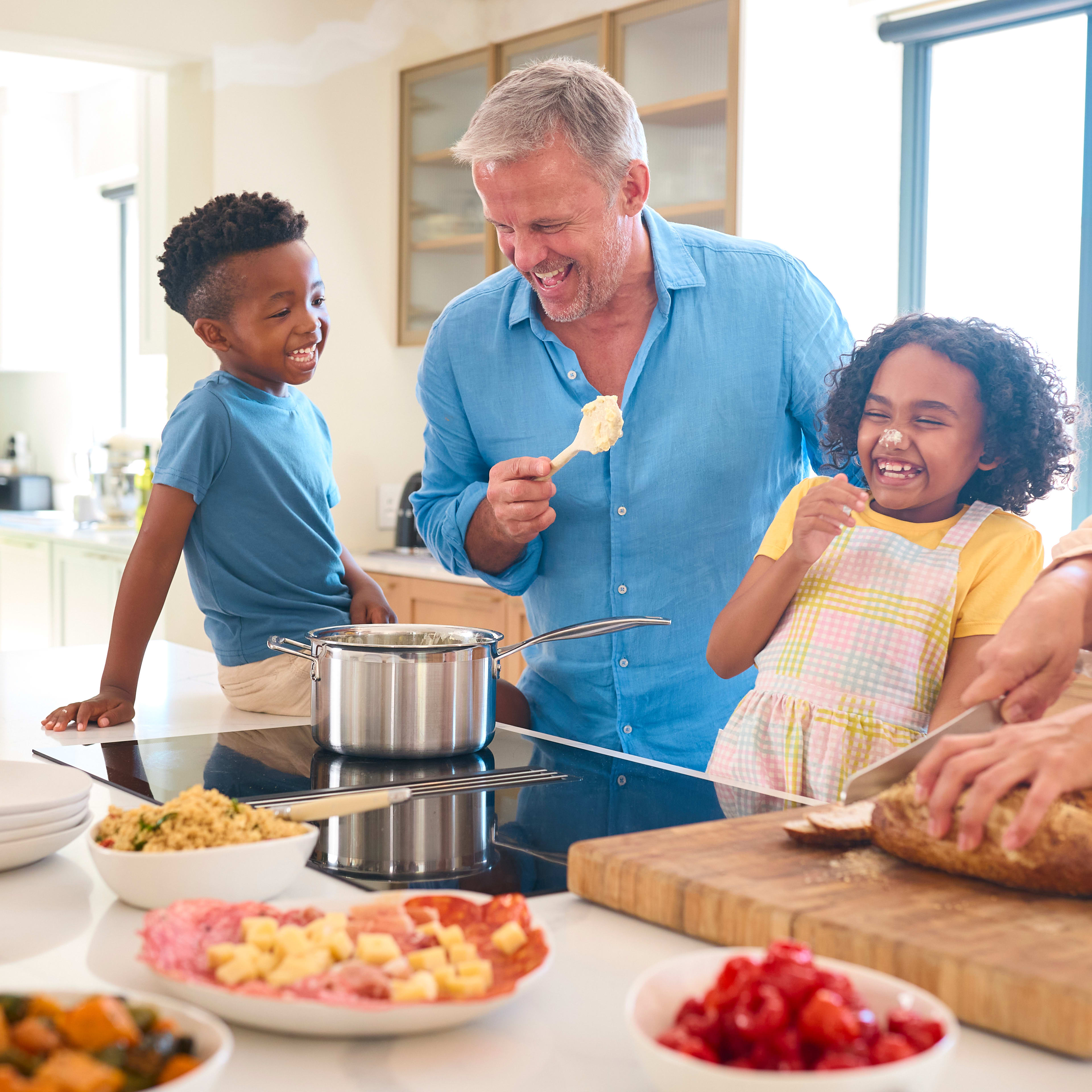 A family of four, including a man, woman, and two children, are gathered in a kitchen, preparing and enjoying a meal together.