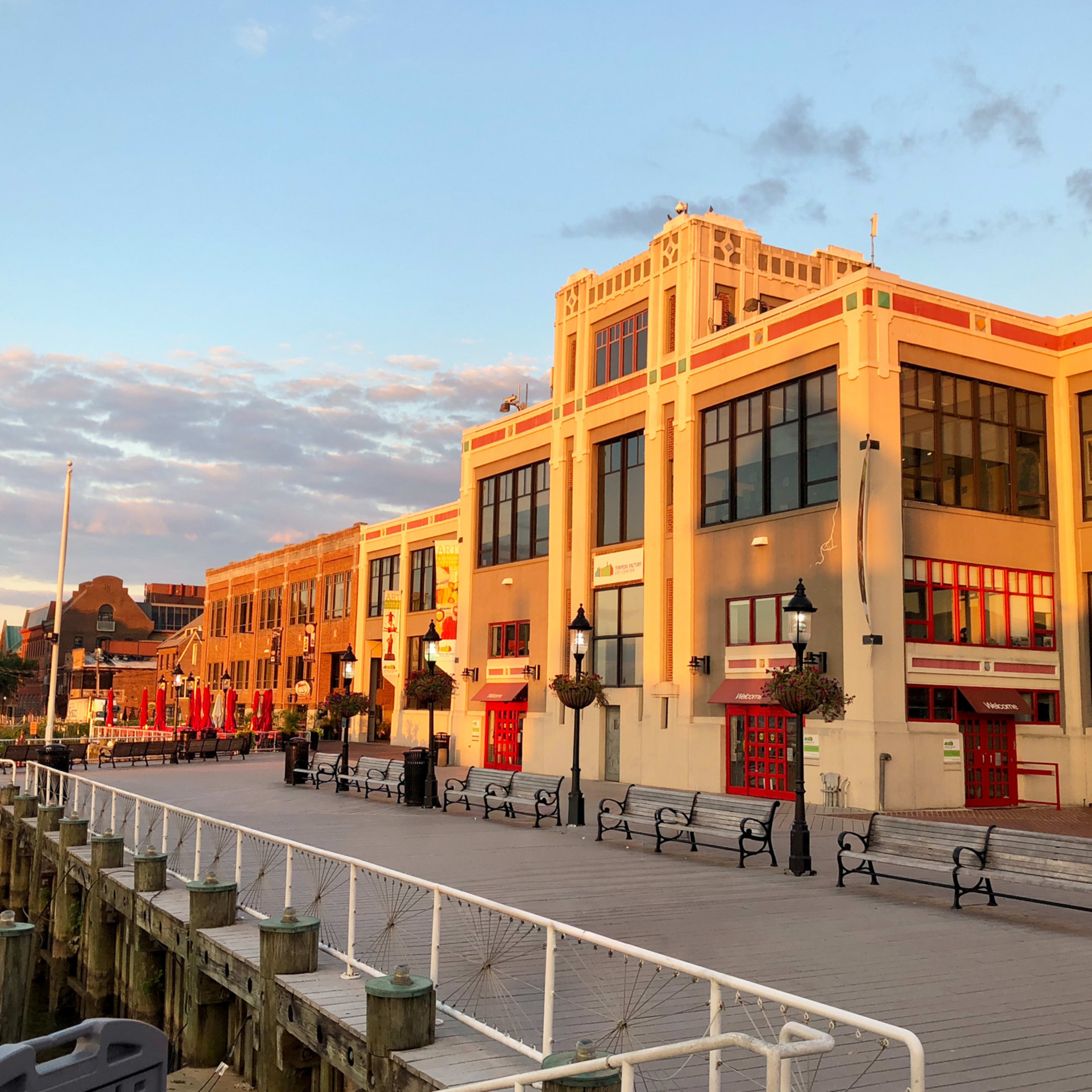 A waterfront promenade lined with colorful, ornate buildings against a backdrop of a cloudy sky at sunset.