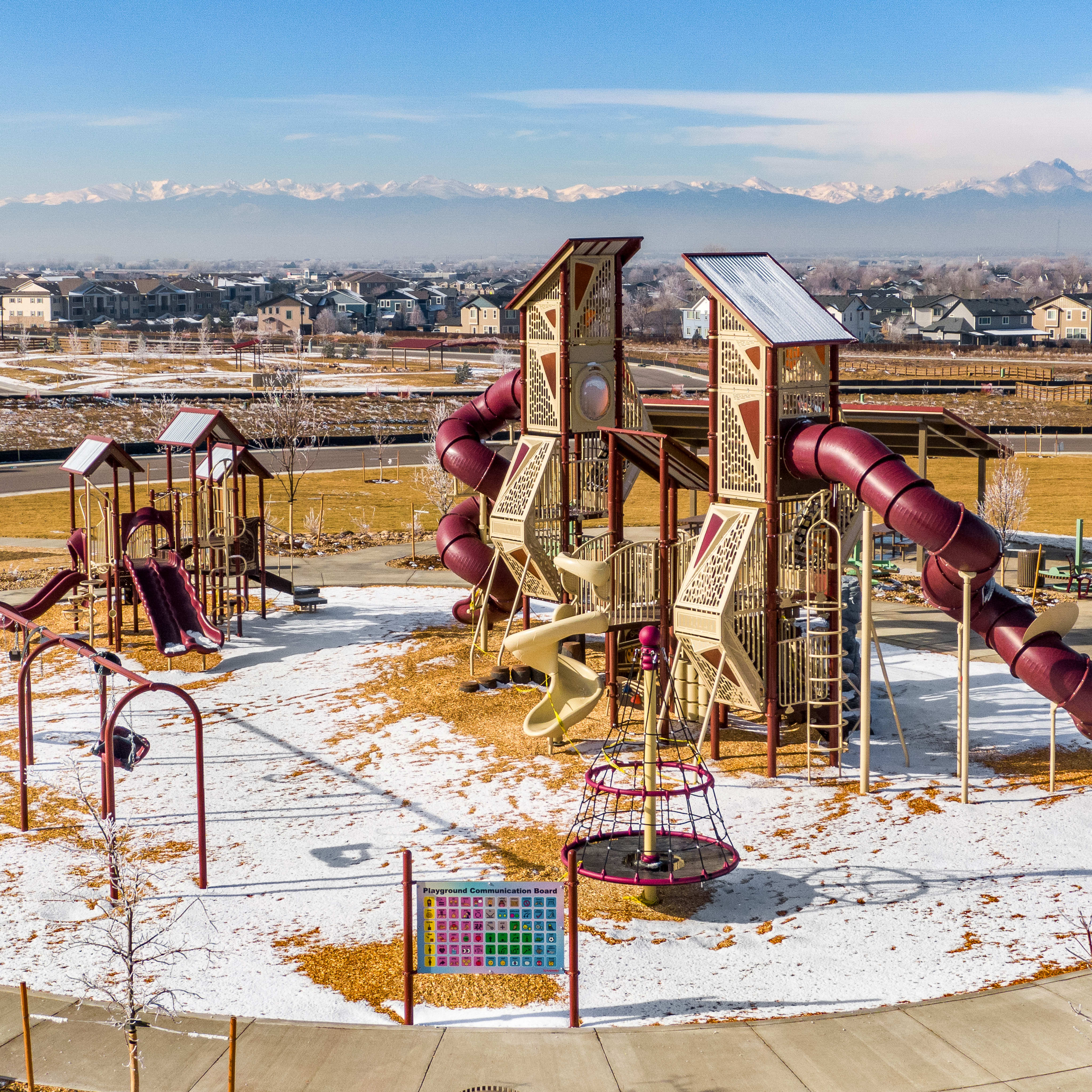A colorful playground with slides and climbing structures stands in the foreground, surrounded by a snowy landscape and a cityscape in the background.