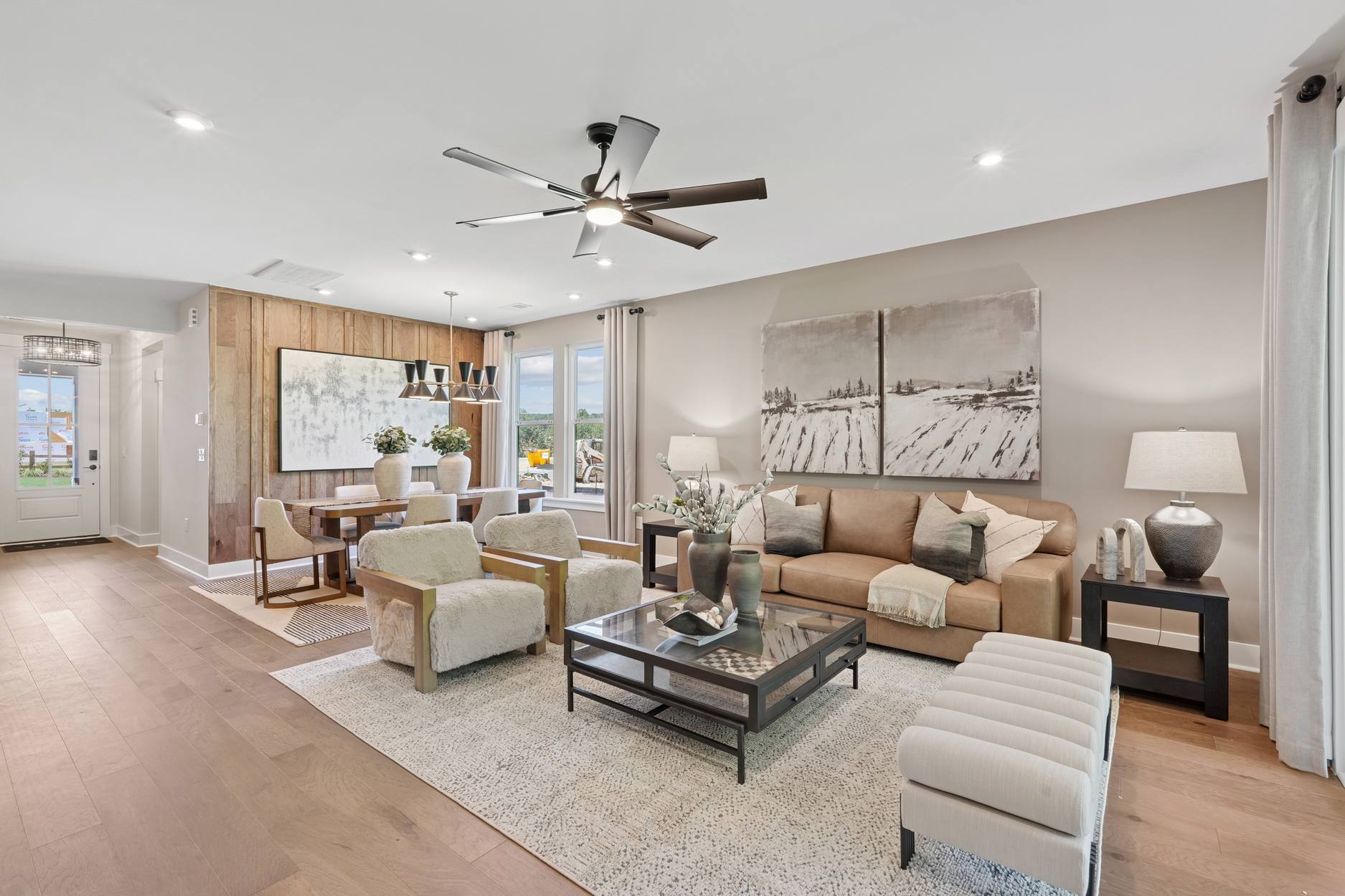 A spacious and well-furnished living room with a ceiling fan, comfortable seating, and a decorative artwork on the wall, creating a warm and inviting atmosphere.