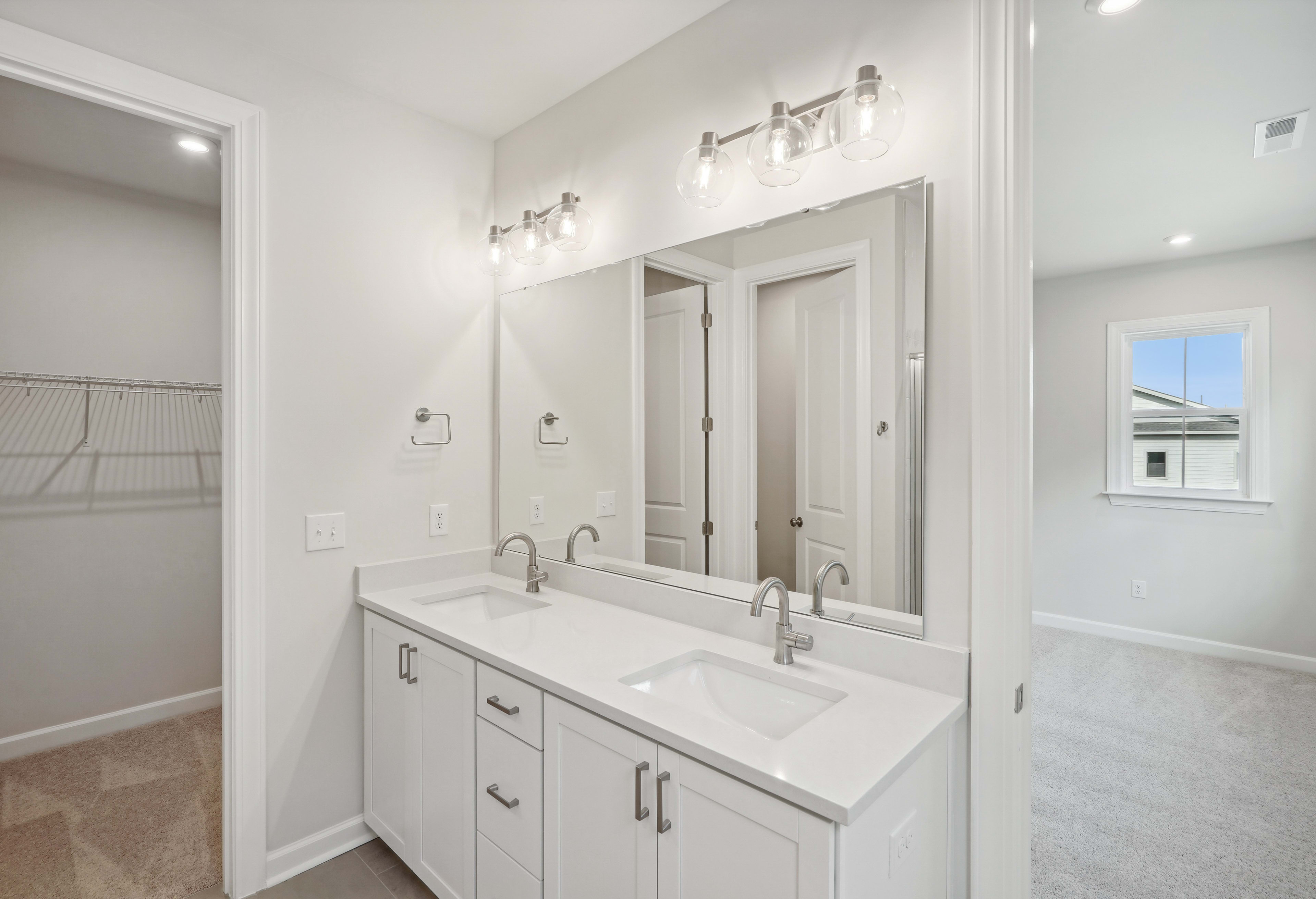 A modern, well-lit bathroom with a double vanity, white cabinets, and a large mirror on the wall.