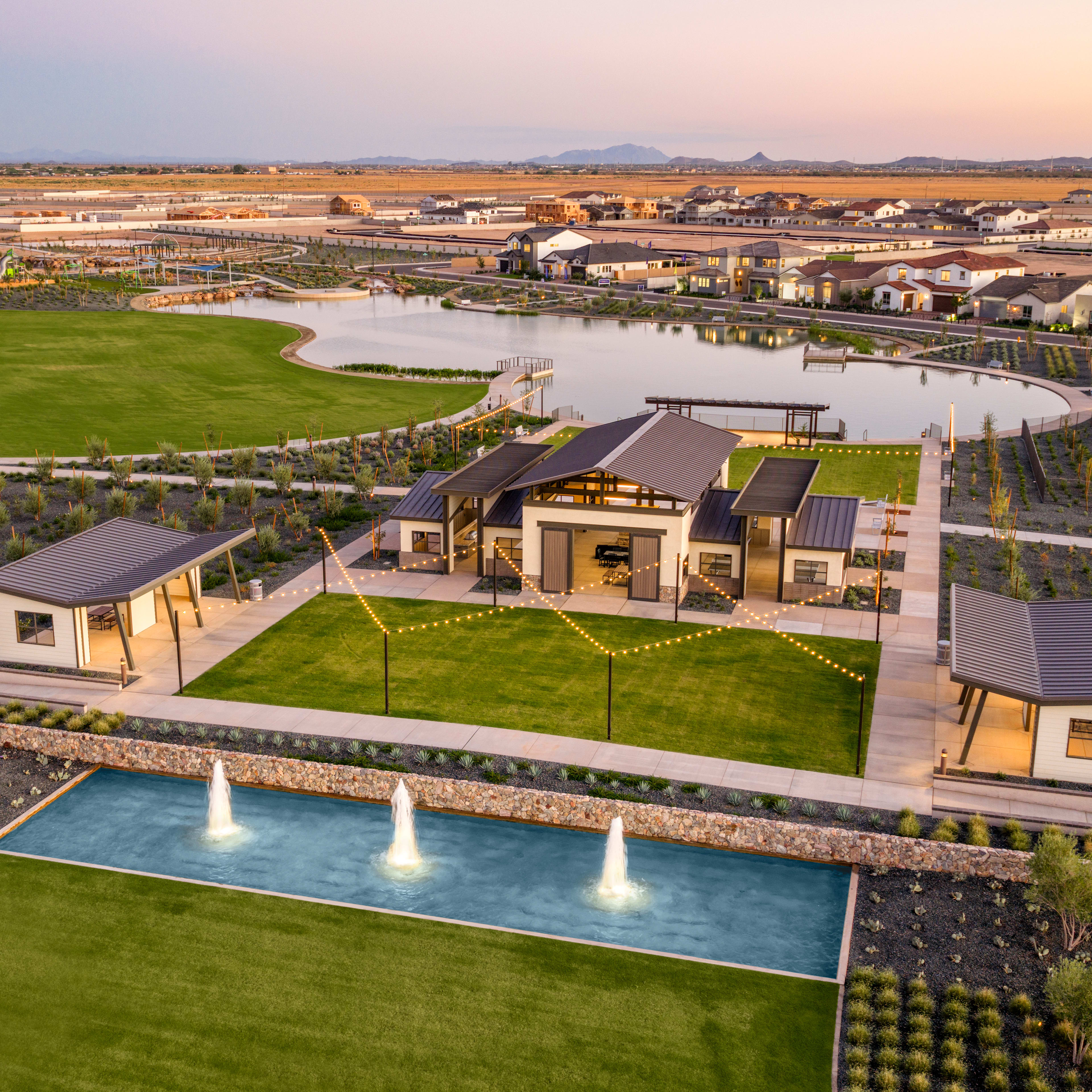 A residential community with a central pool and landscaped grounds, surrounded by a vast expanse of desert landscape and mountains in the distance.