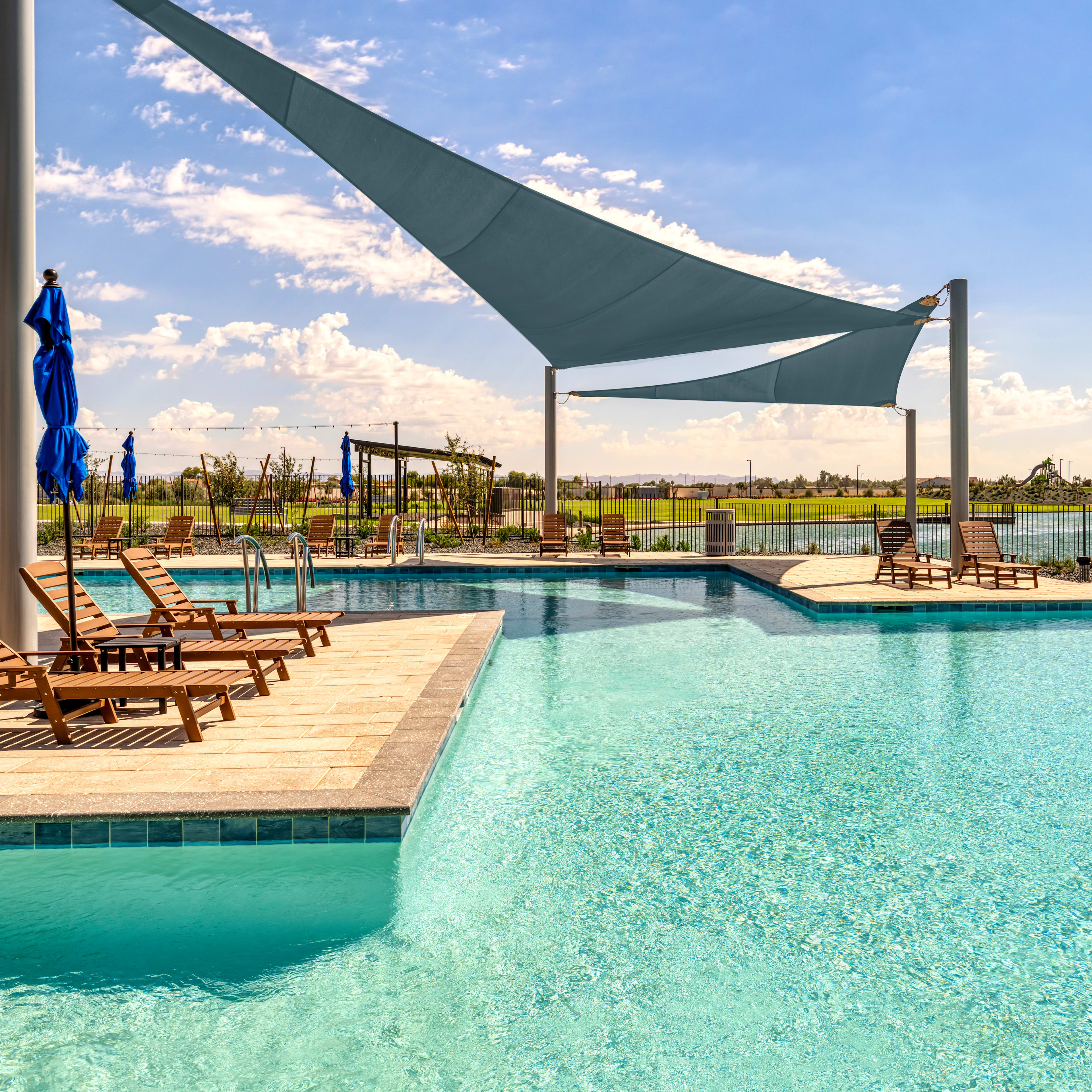 A serene outdoor pool surrounded by lounge chairs and shaded by large, triangular canopies, with a scenic landscape visible in the background.
