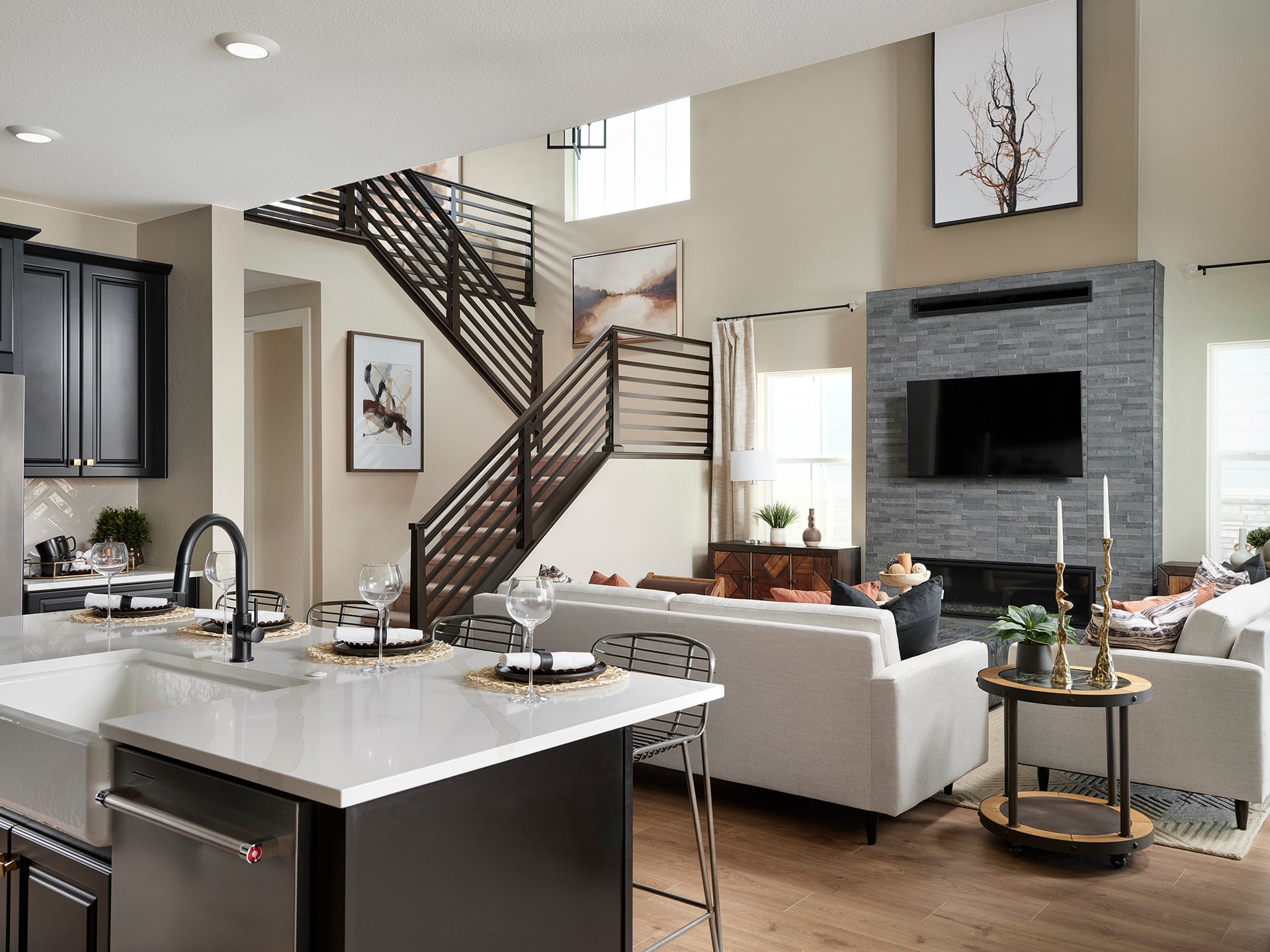A modern and open-concept living space with a kitchen island, a fireplace, and a staircase with a unique railing design, all set against a neutral color palette and accented with decorative elements.