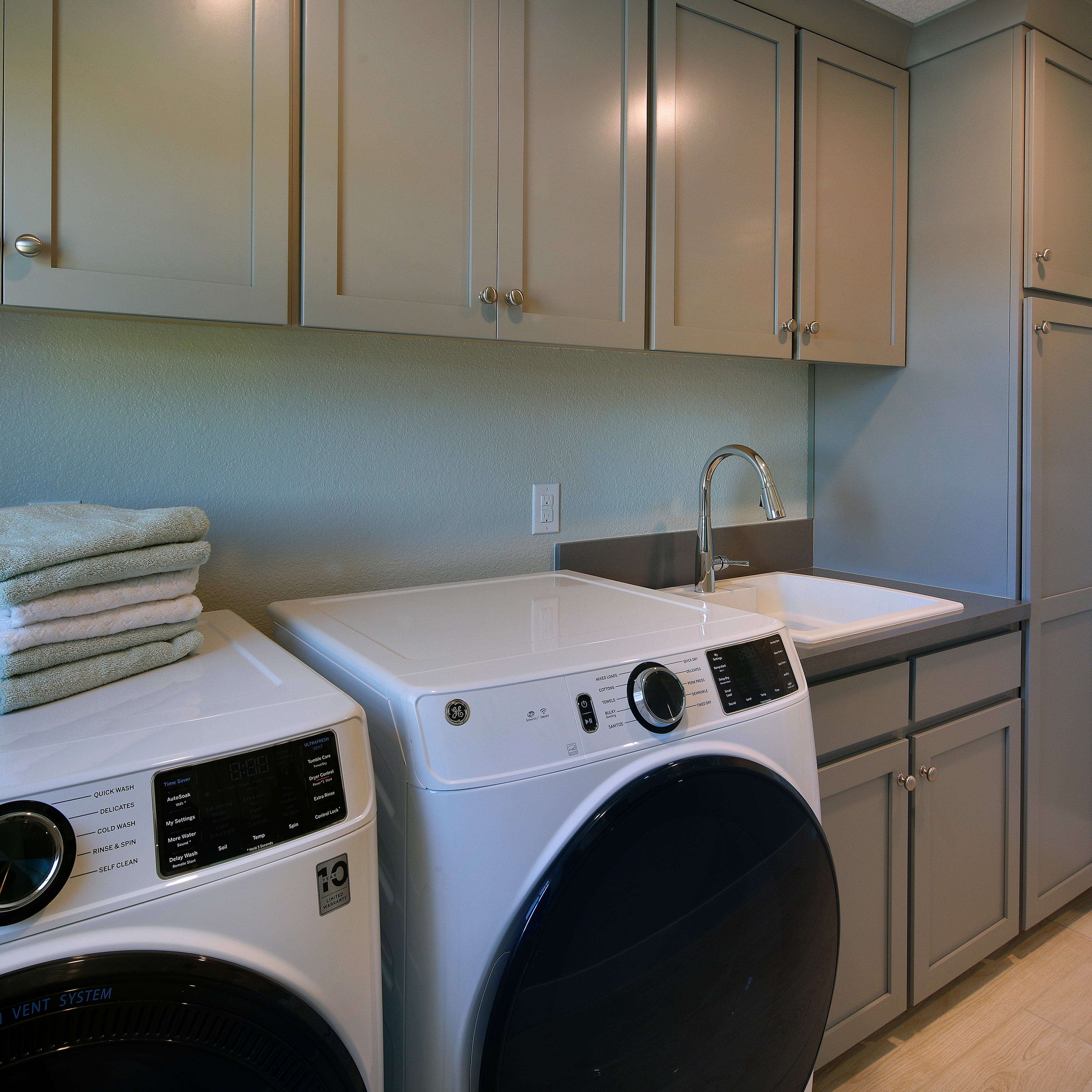 A modern and well-equipped laundry room with a washing machine, dryer, and cabinets for storage, along with neatly folded towels on the counter.