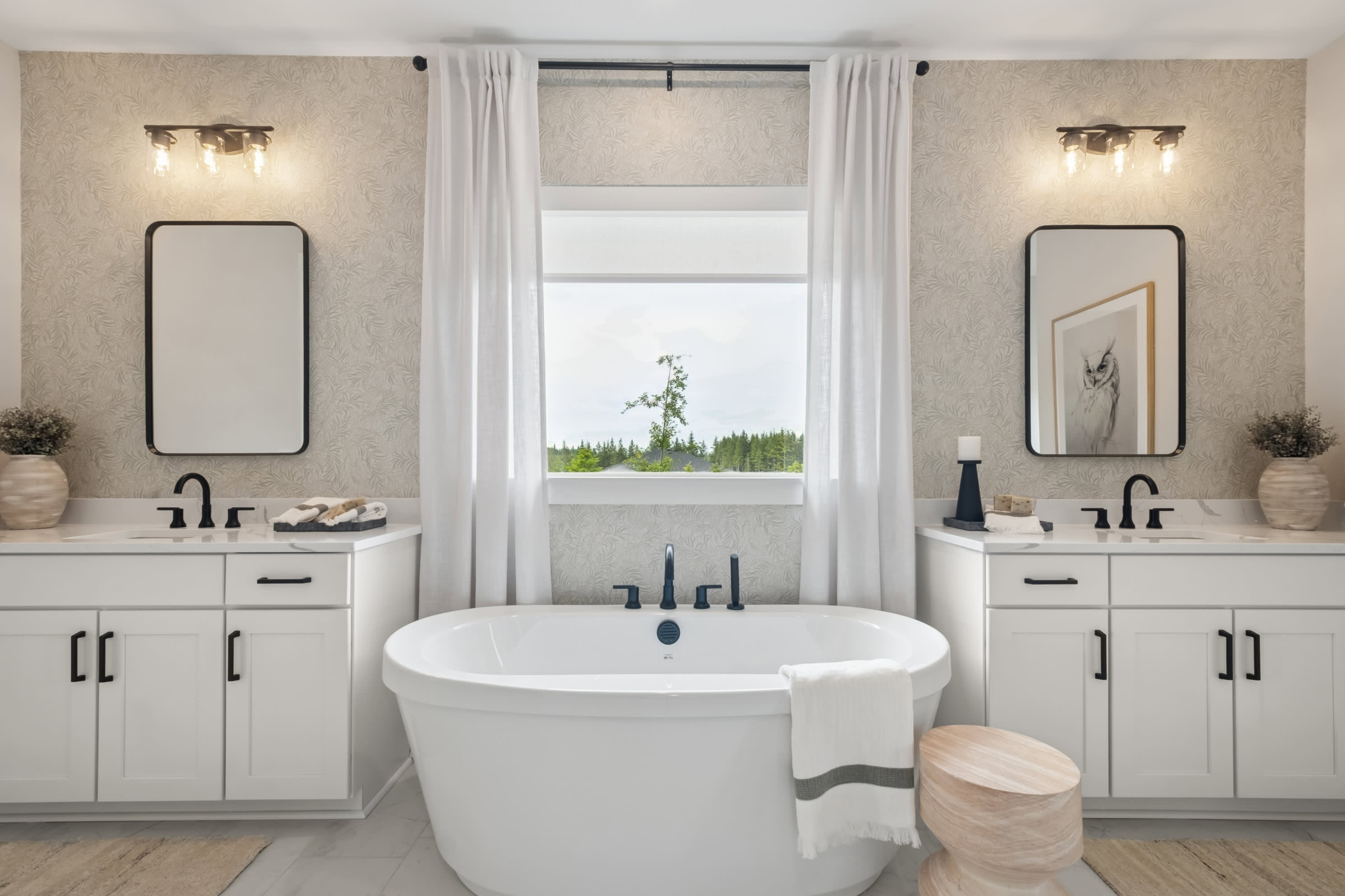 A spacious and well-designed bathroom with a freestanding bathtub, double vanity, and large window overlooking a lush outdoor landscape.