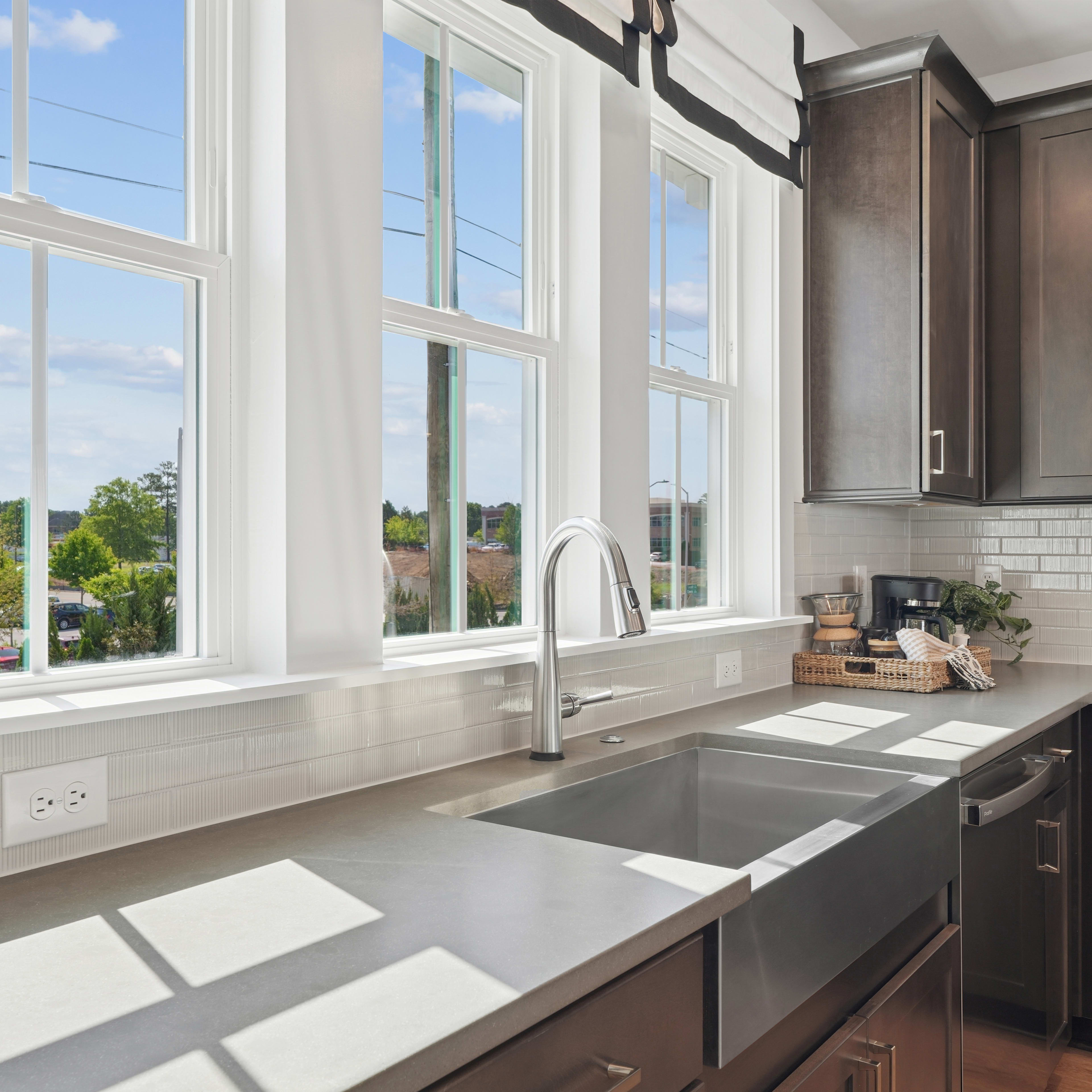 A modern kitchen with large windows overlooking a scenic outdoor landscape, featuring dark wood cabinets, a stainless steel sink, and a bright, airy atmosphere.