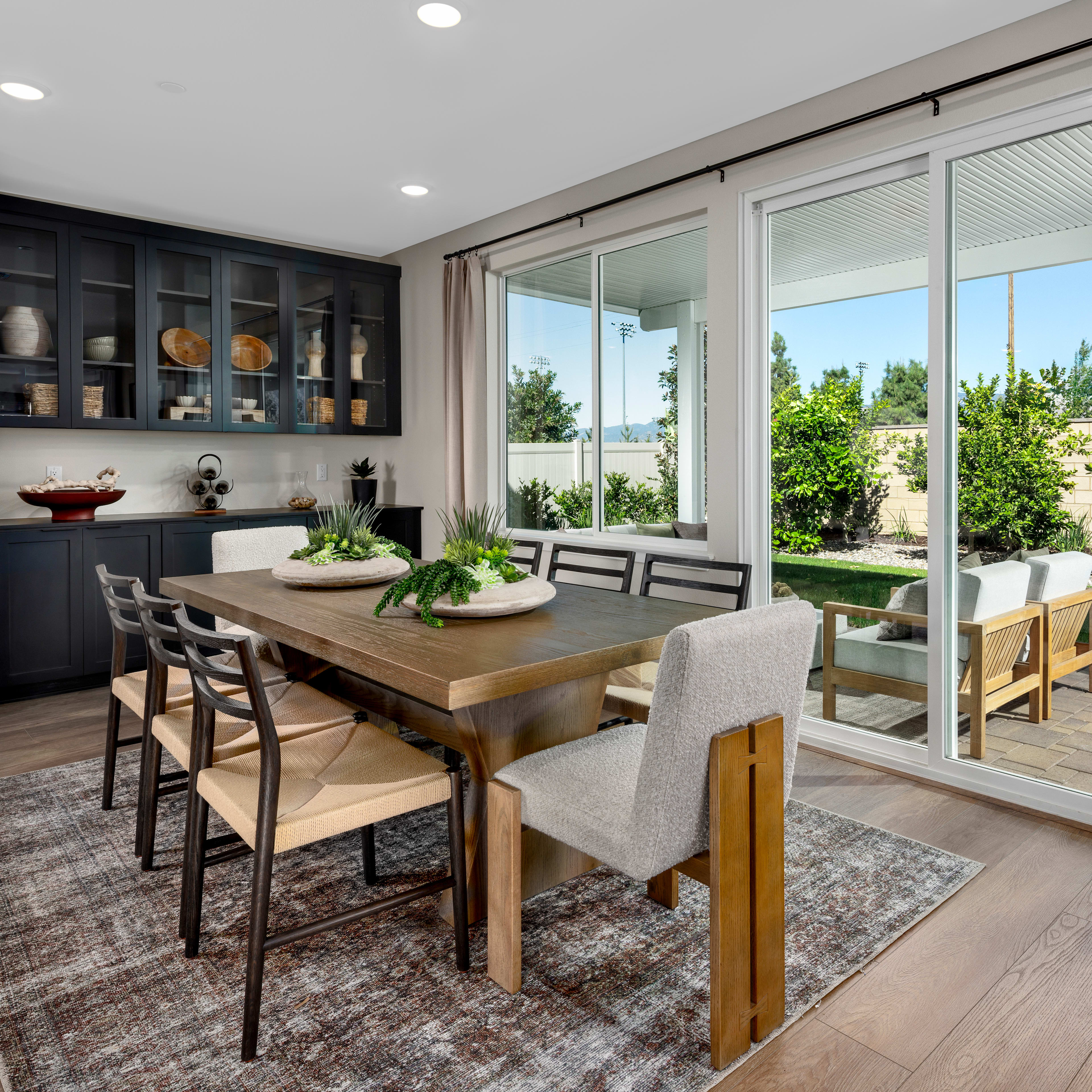 A modern and spacious dining area with a wooden table, upholstered chairs, and a large window overlooking a lush outdoor landscape.