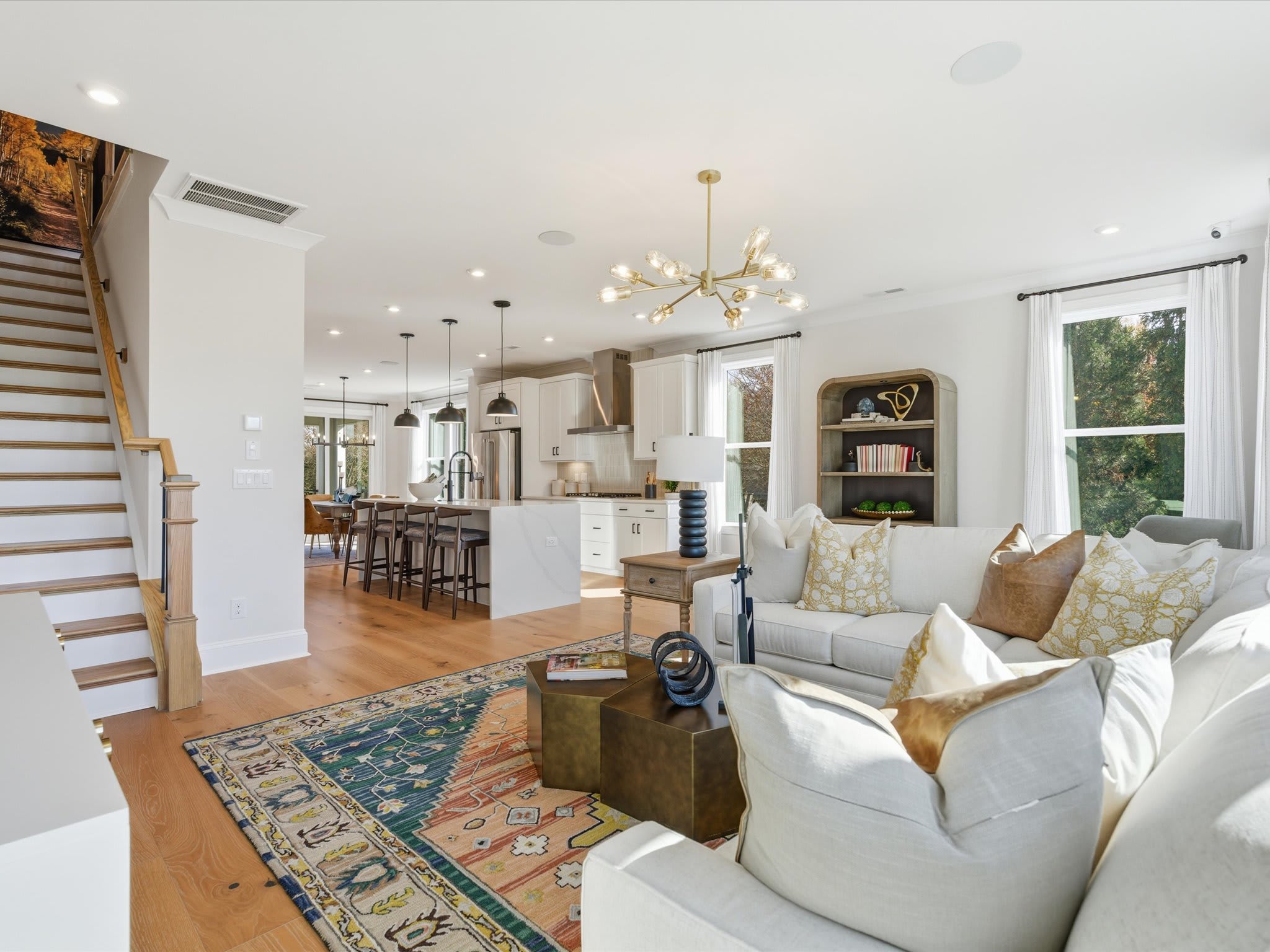 A spacious and well-furnished living room with a cozy seating area, a kitchen with modern appliances, and a wooden staircase leading to an upper level.