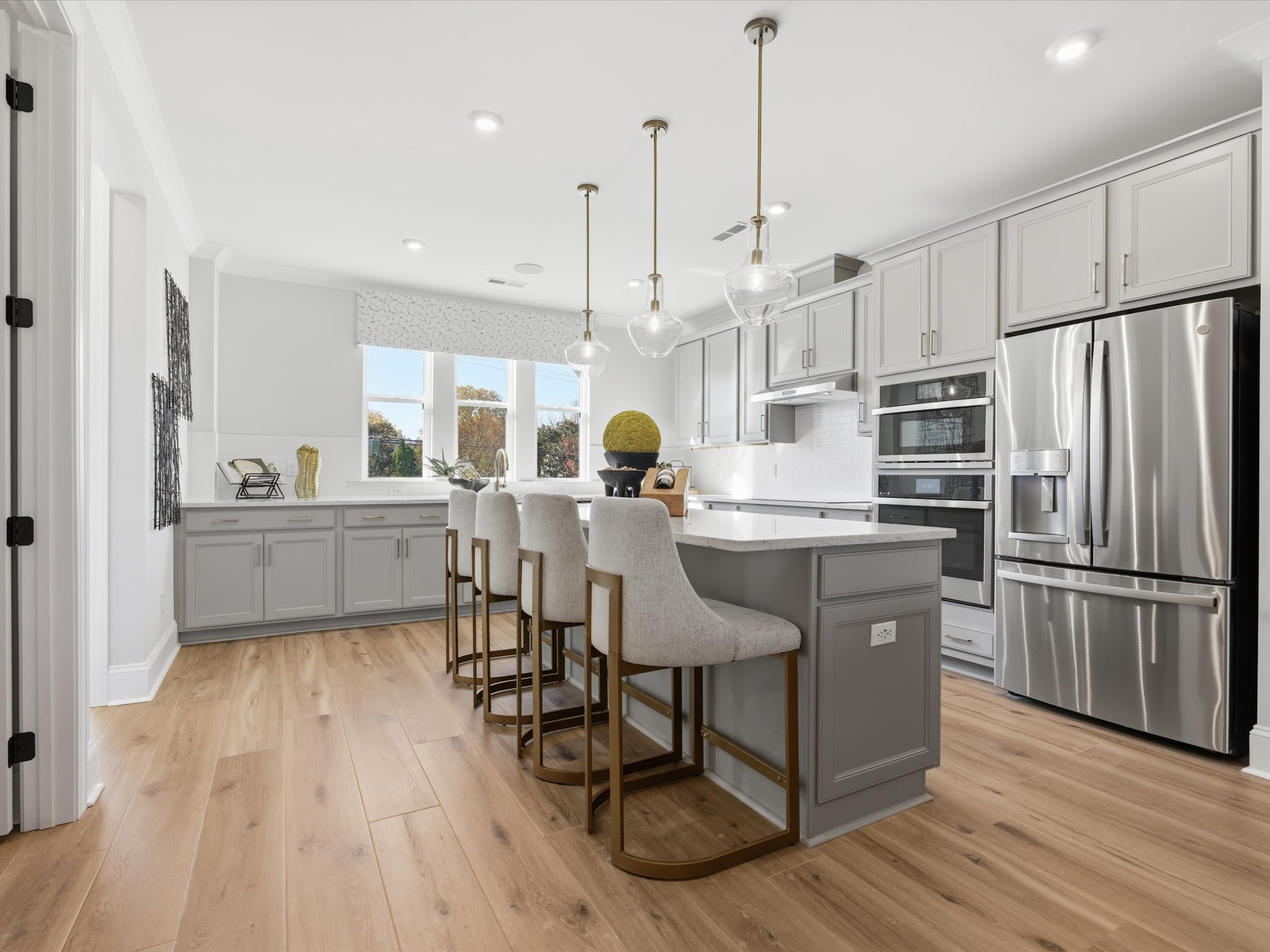 A modern, open-concept kitchen with white cabinets, gray island, stainless steel appliances, and hardwood floors, featuring pendant lighting and bar stools.