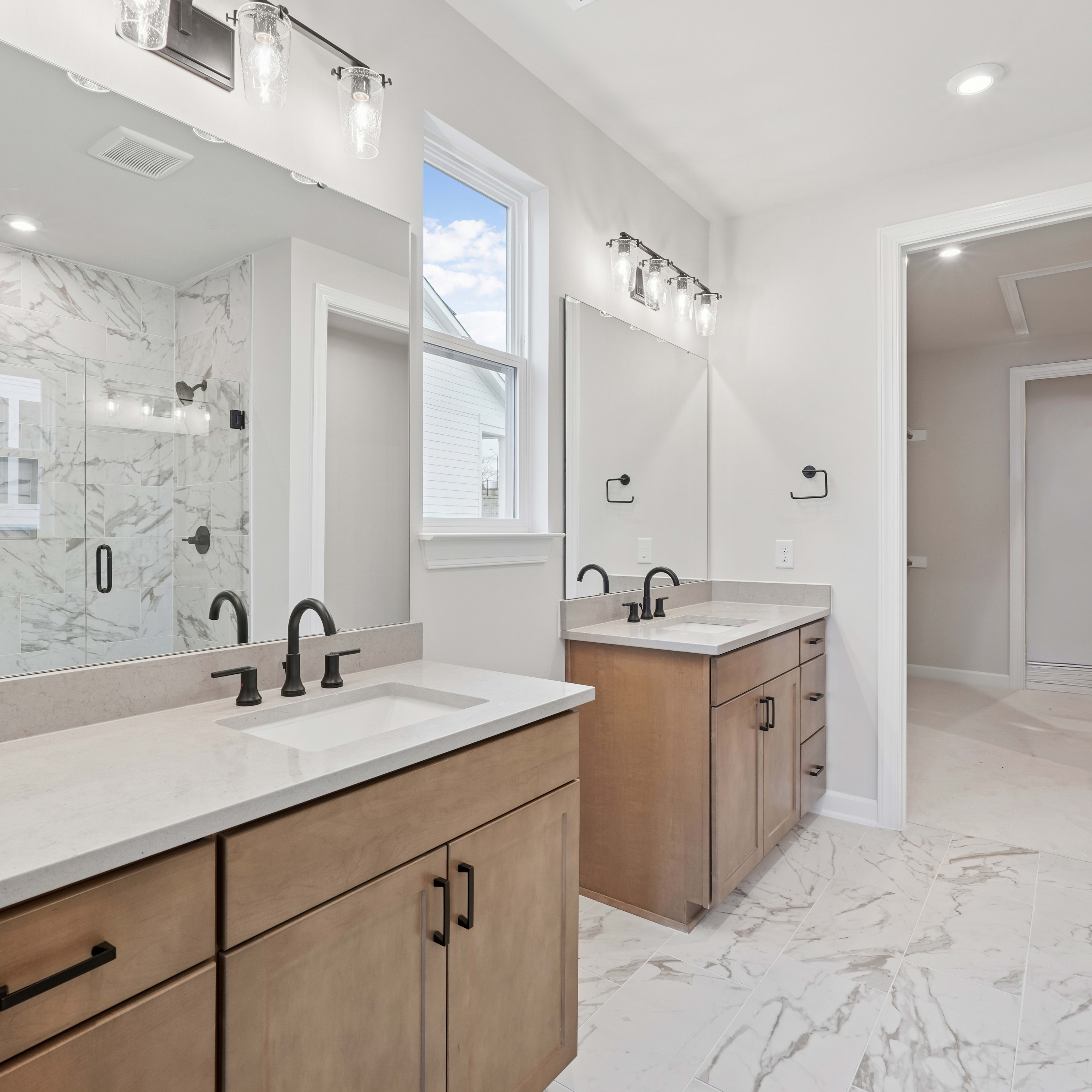 A spacious and modern bathroom with a double vanity, marble countertops, and a large window providing natural light.