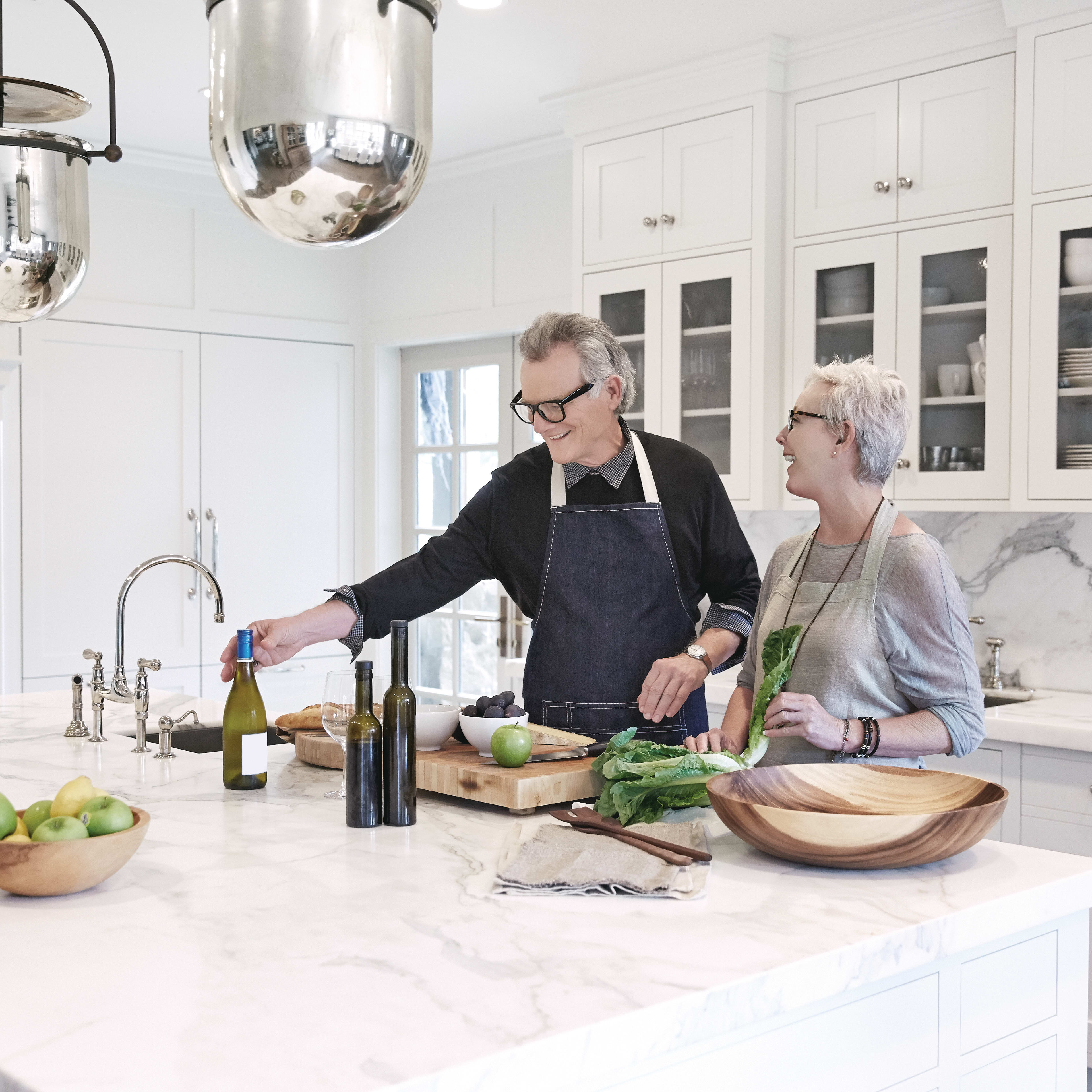 A modern, well-equipped kitchen with two people, a man and a woman, working together to prepare a meal, surrounded by various kitchen appliances and ingredients.