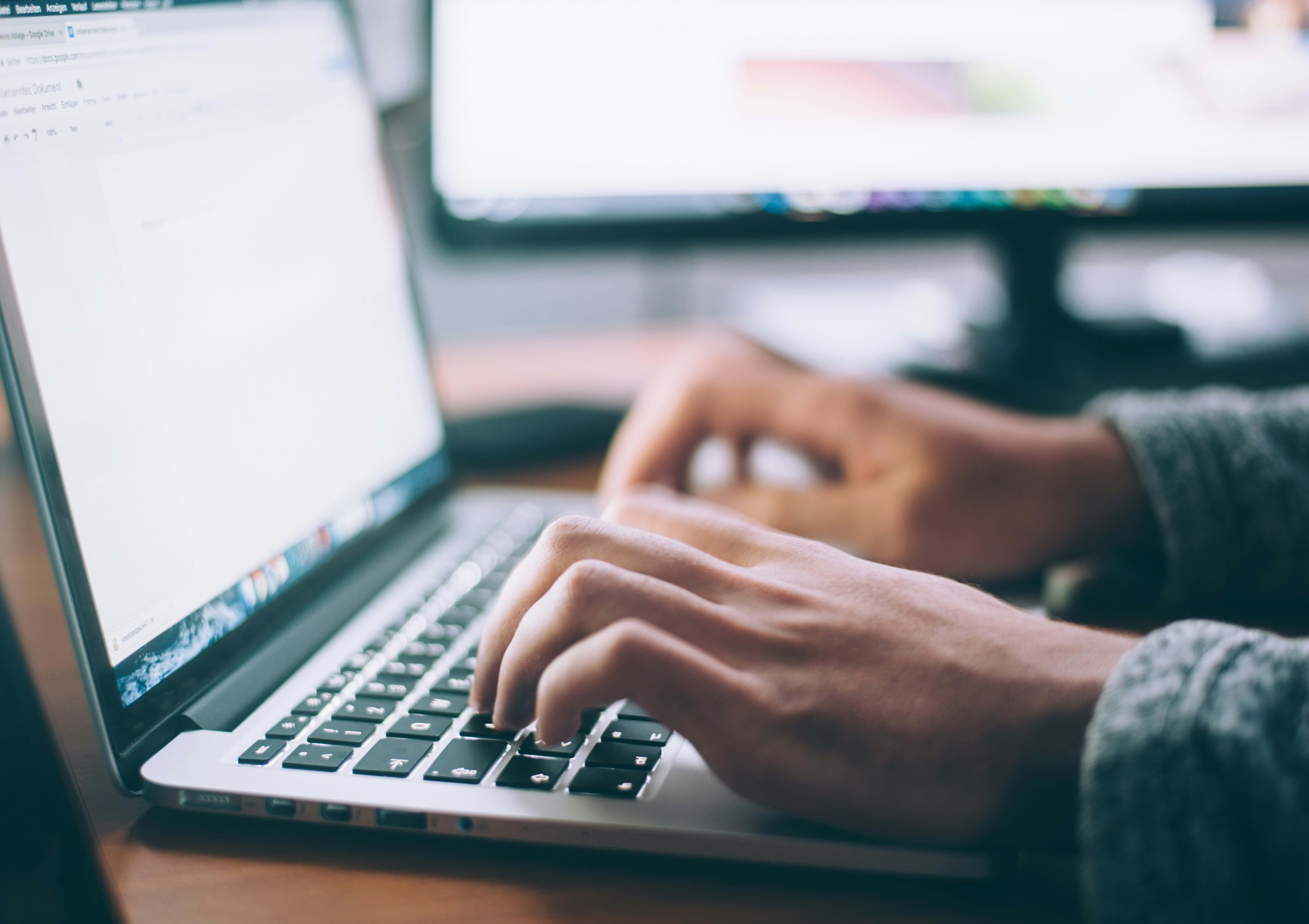 The image shows a person's hands typing on a laptop keyboard, with a blurred computer screen visible in the background.