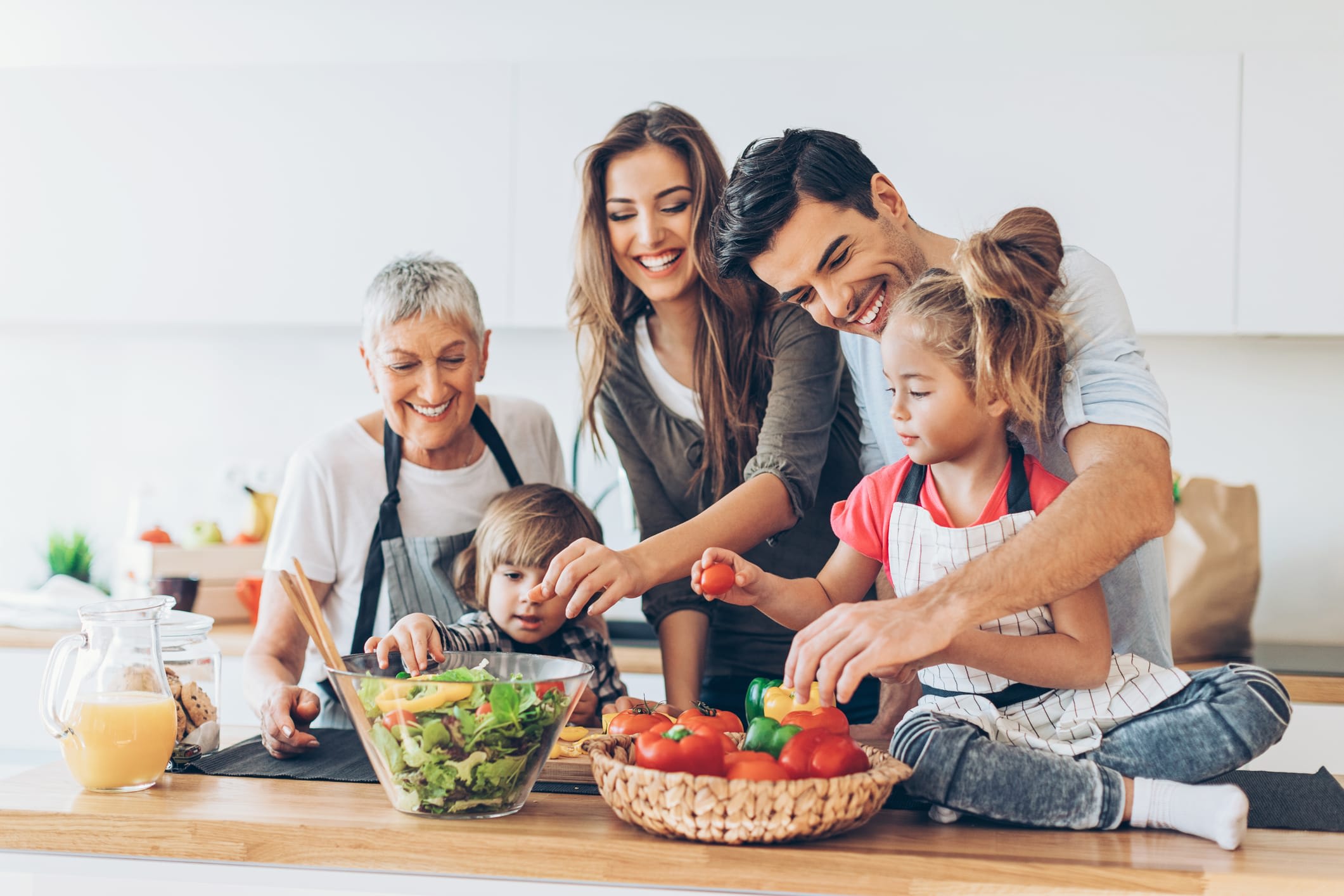 A happy family is gathered in the kitchen, preparing a healthy meal together while smiling and interacting with each other.