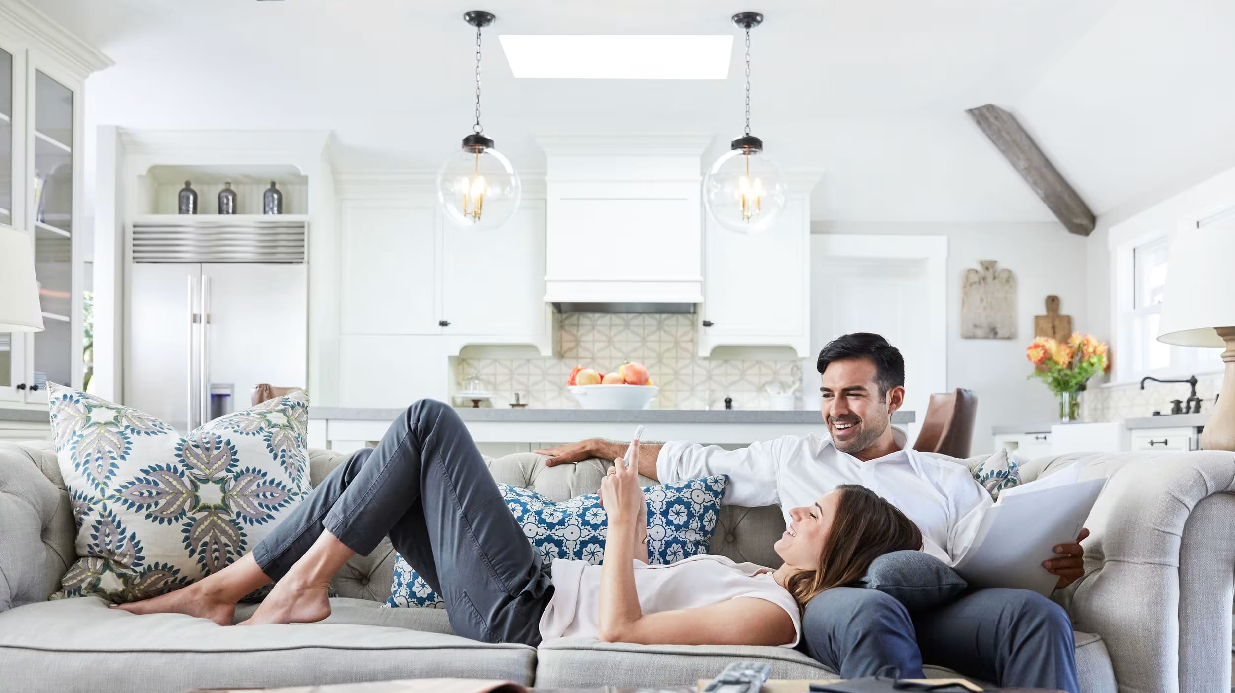 The image depicts a cozy living room with a couple relaxing on a comfortable couch, surrounded by modern decor and lighting fixtures.