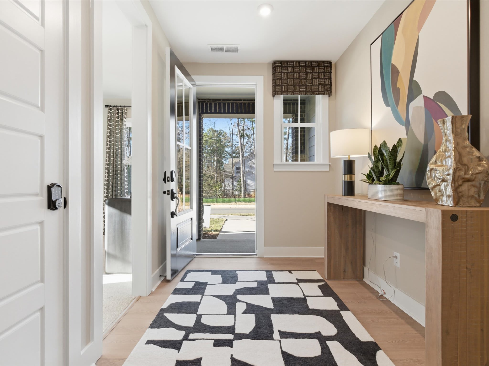 A bright and airy entryway with a patterned rug, a wooden console table, and a large window overlooking a scenic outdoor view.