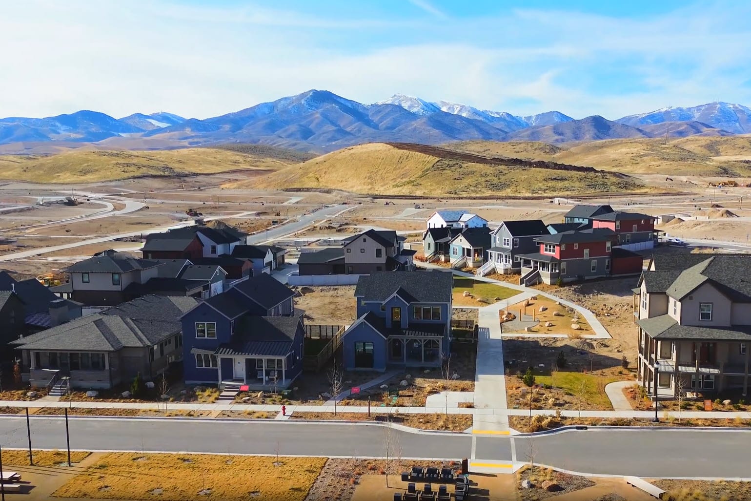 A residential neighborhood nestled in a mountainous landscape, with colorful houses and a winding road leading through the hilly terrain.