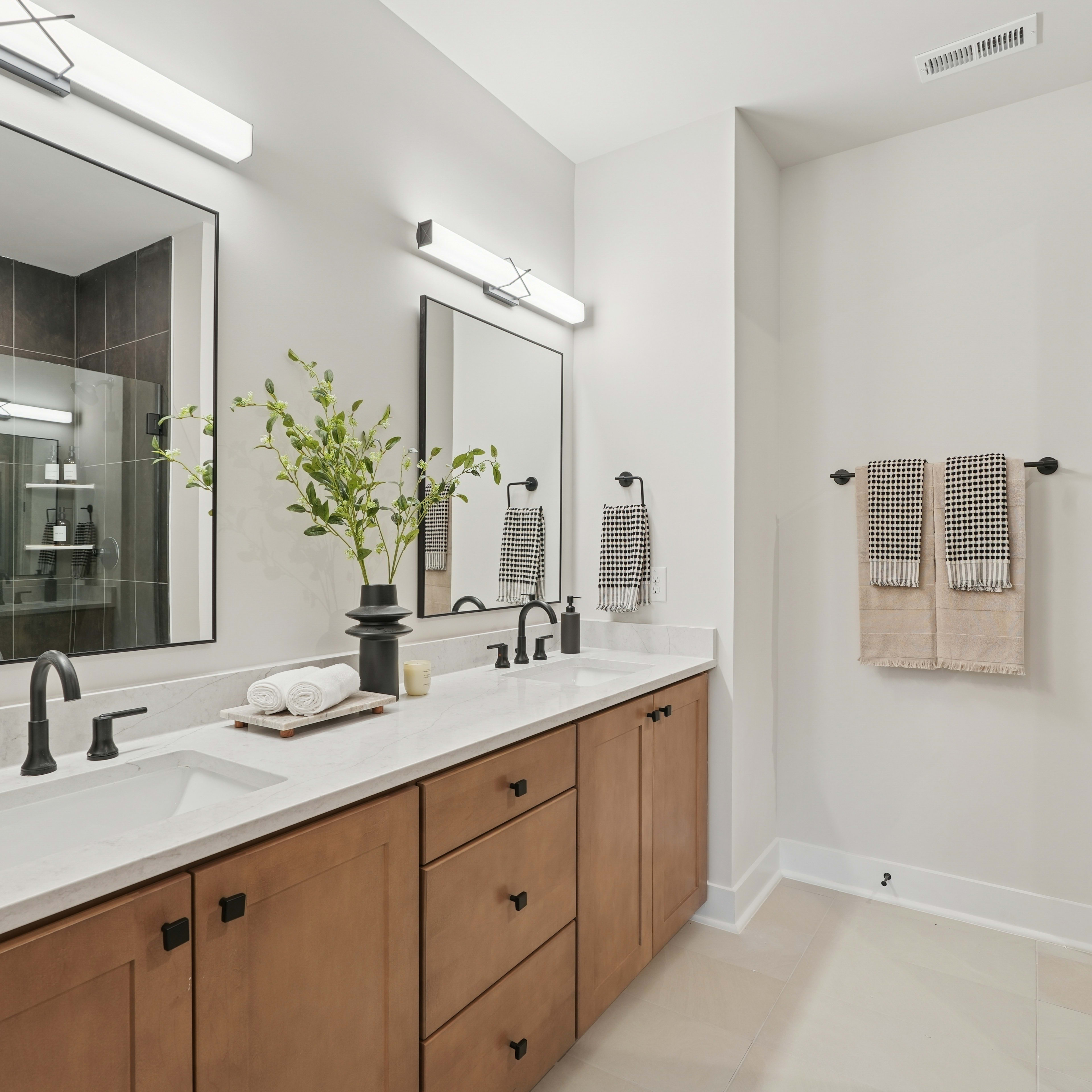 A modern and minimalist bathroom with a double vanity, a large mirror, and a glass shower enclosure, complemented by natural wood cabinetry and neutral-toned decor.