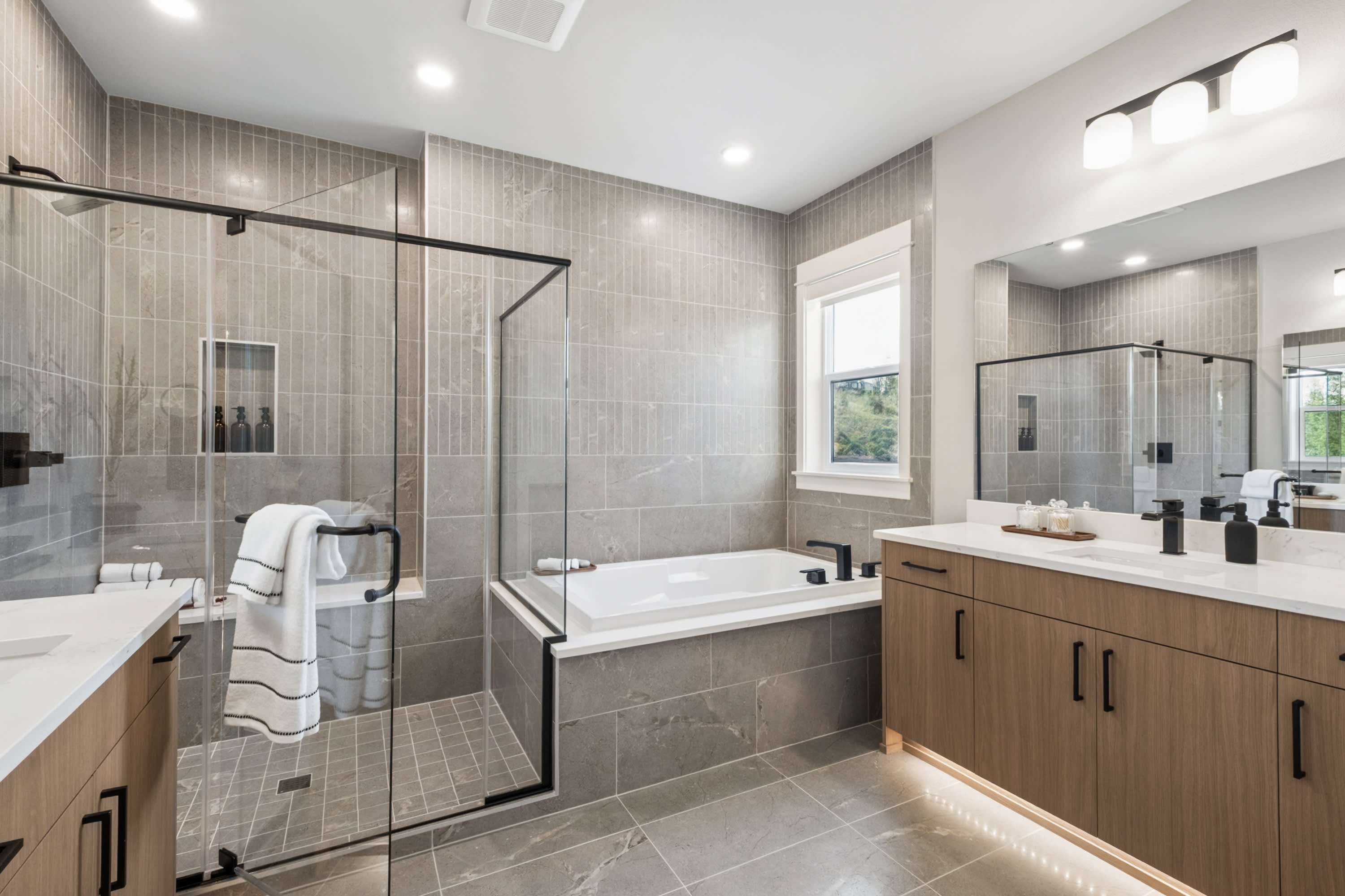 A modern and spacious bathroom with a large shower enclosure, a bathtub, and a wooden vanity with a white countertop.