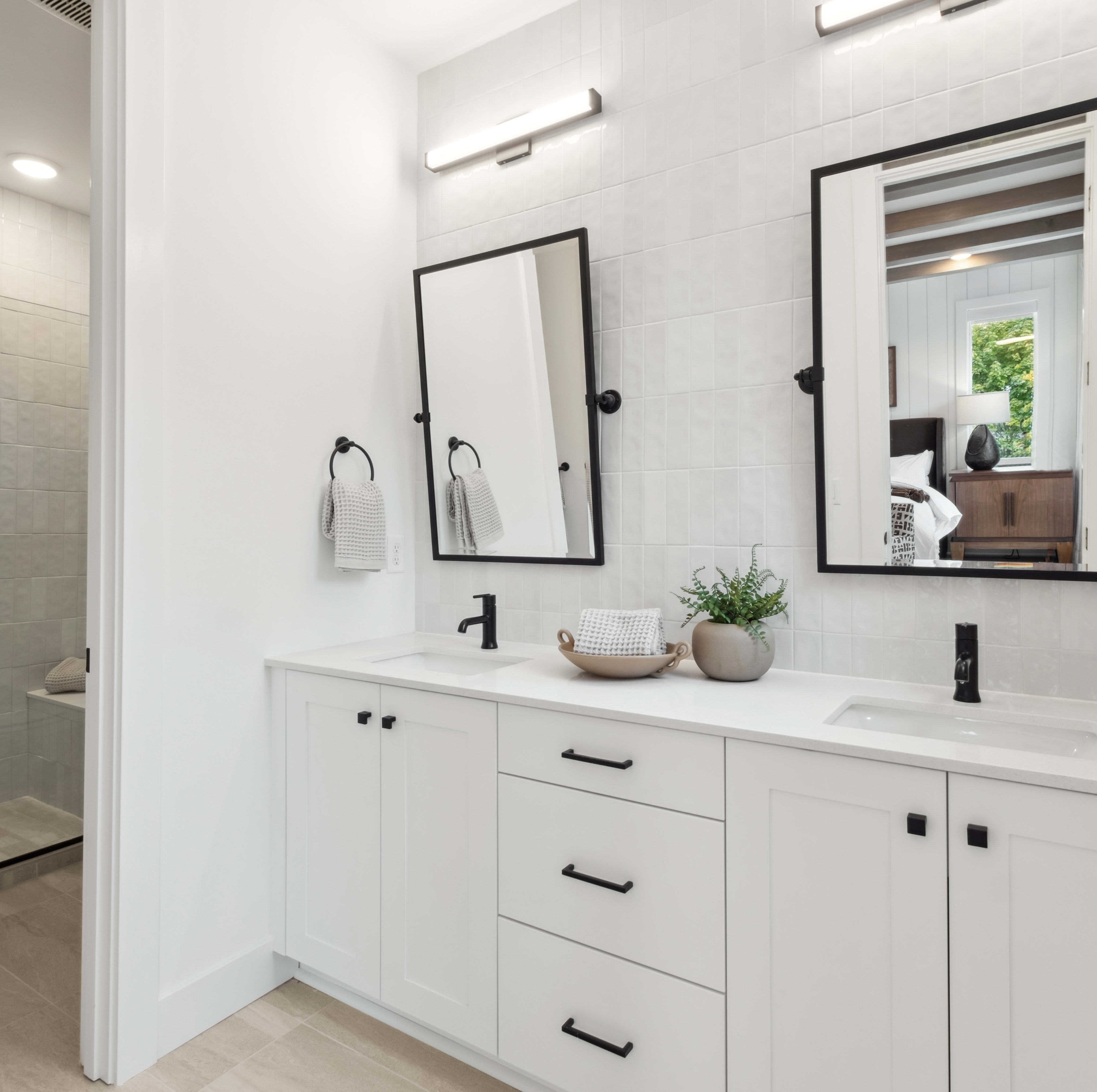 A modern, minimalist bathroom with a white vanity, framed mirrors, and a glass shower enclosure, set against a bright and airy backdrop.
