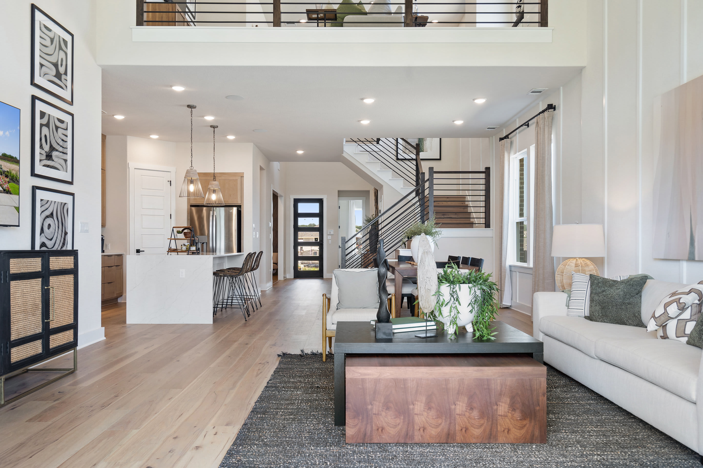 A modern and open-concept living space with a cozy seating area, a wooden coffee table, and a staircase leading to an upper level, all set against a backdrop of white walls and hardwood floors.