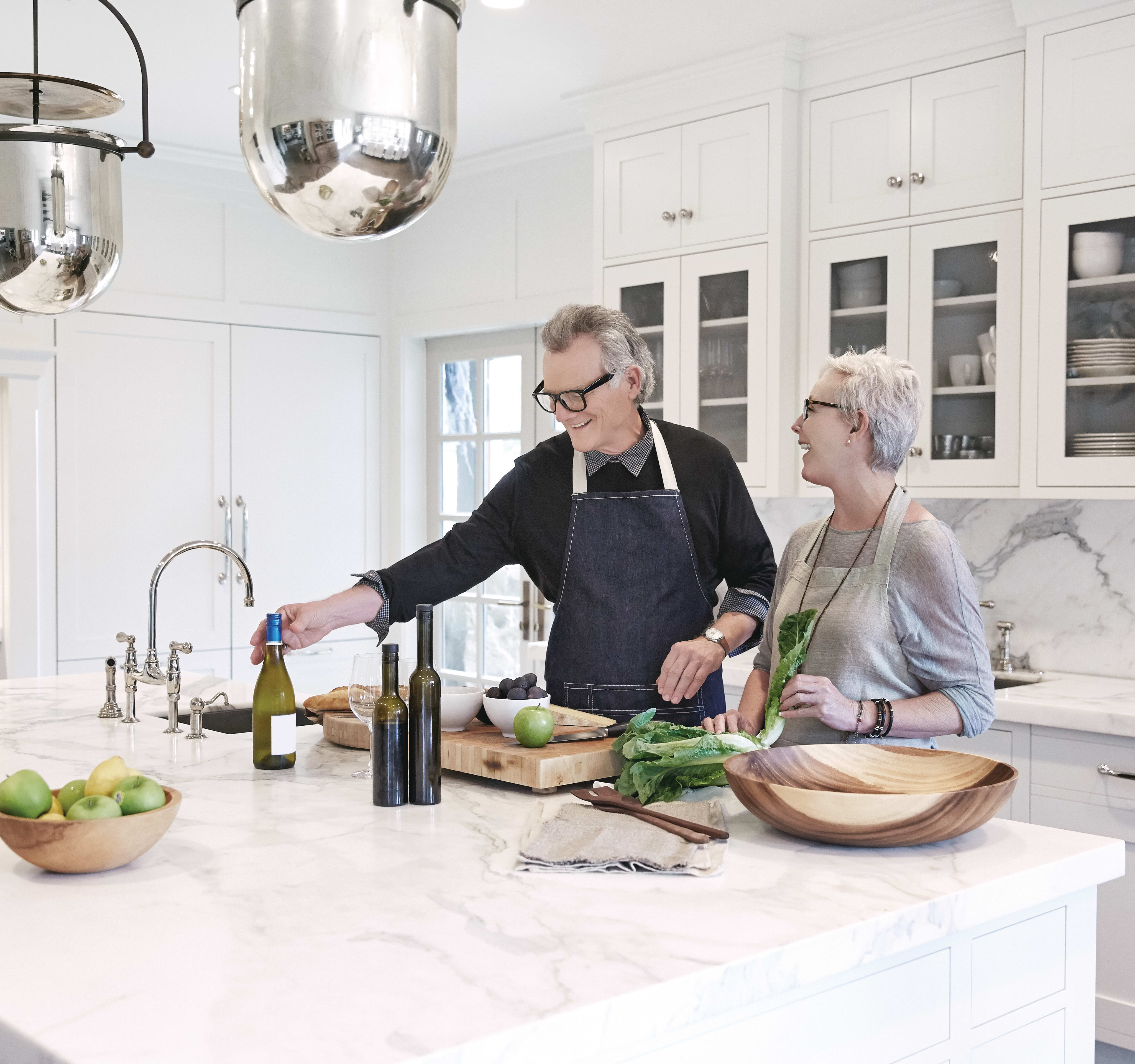 A modern, well-equipped kitchen with two people, a man and a woman, working together to prepare a meal, surrounded by various kitchen appliances and ingredients.