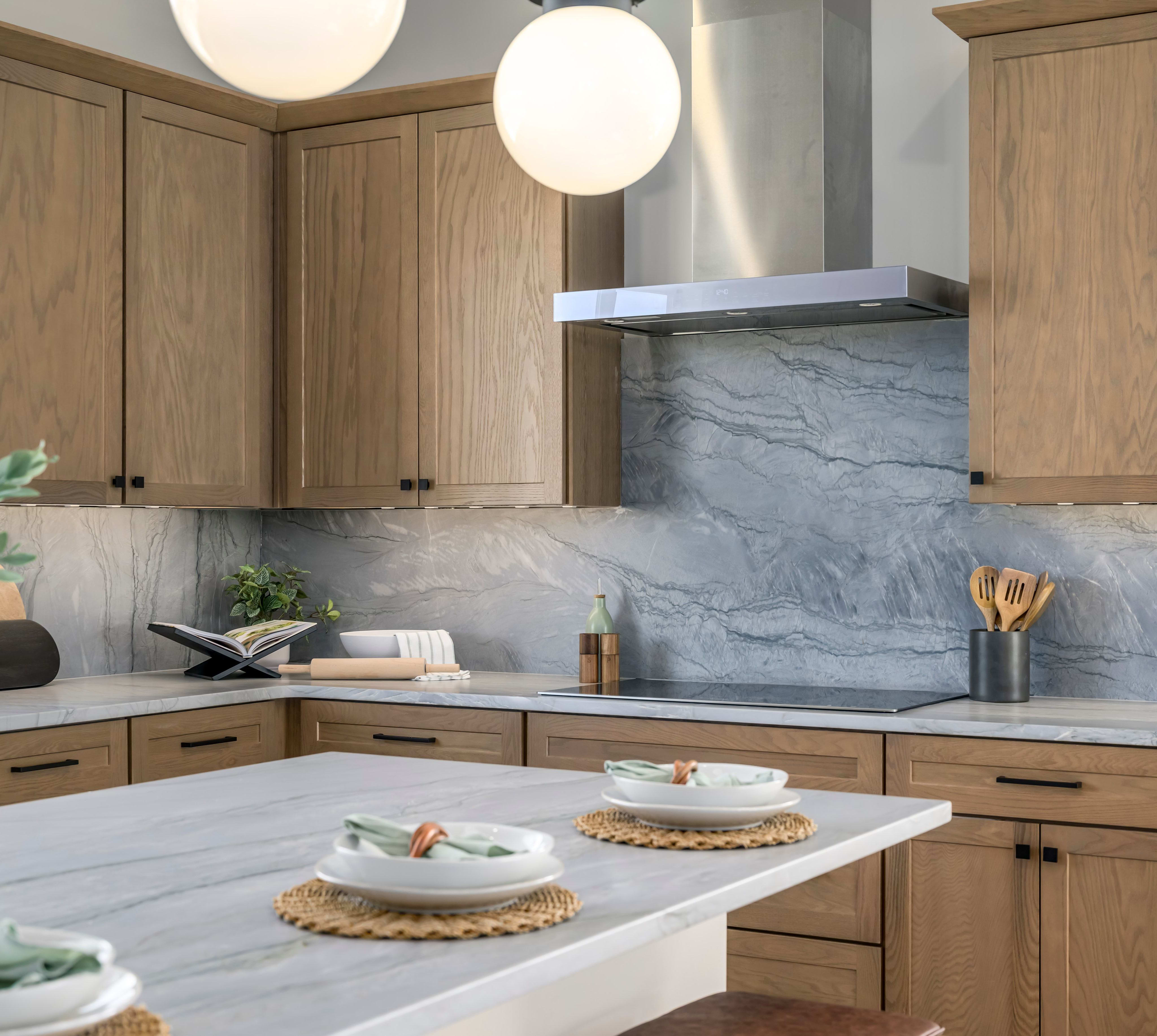 A modern and minimalist kitchen with wooden cabinets, a marble backsplash, and a central island with baked goods displayed on it.
