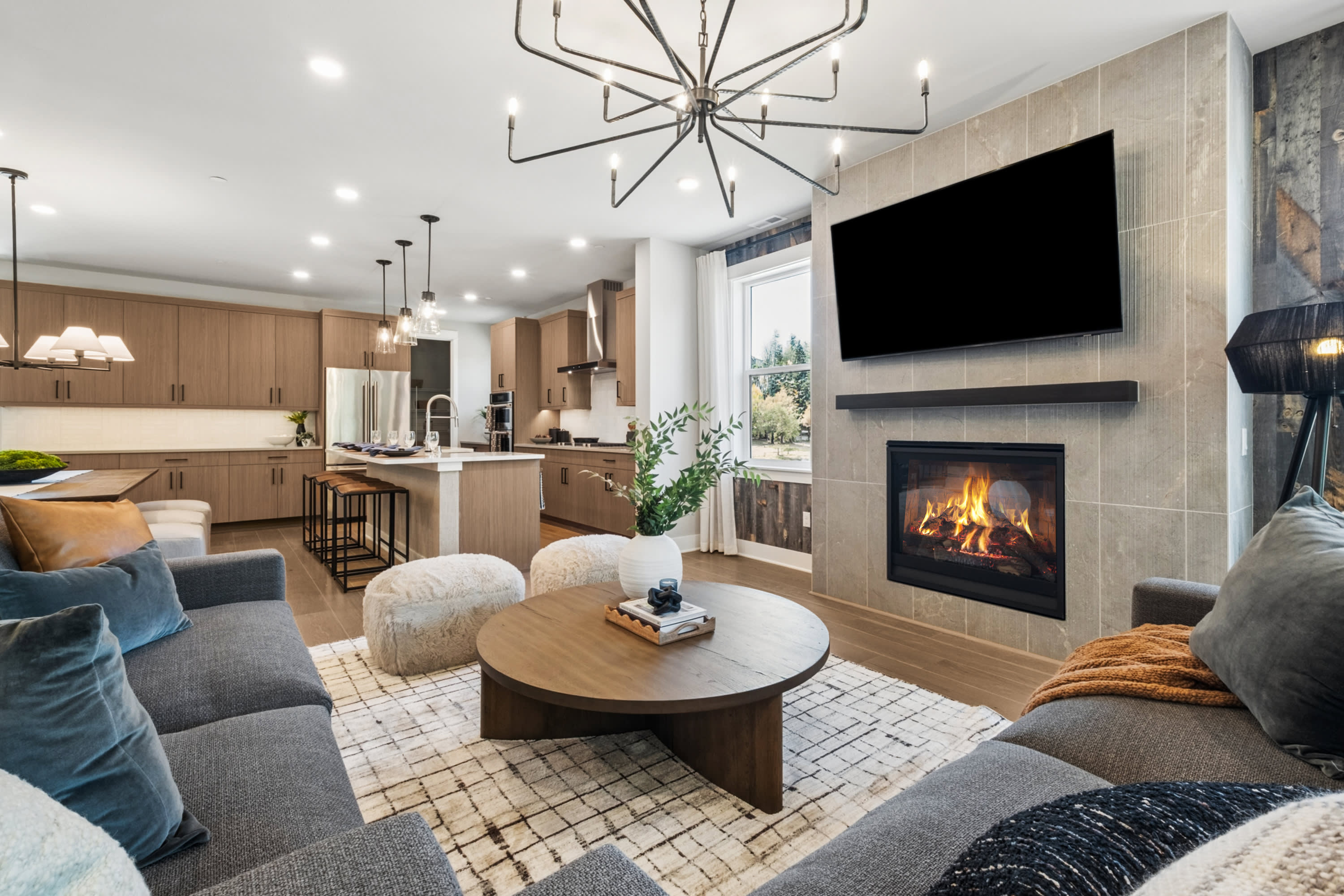 A cozy and modern living room with a fireplace, comfortable seating, and a kitchen visible in the background.