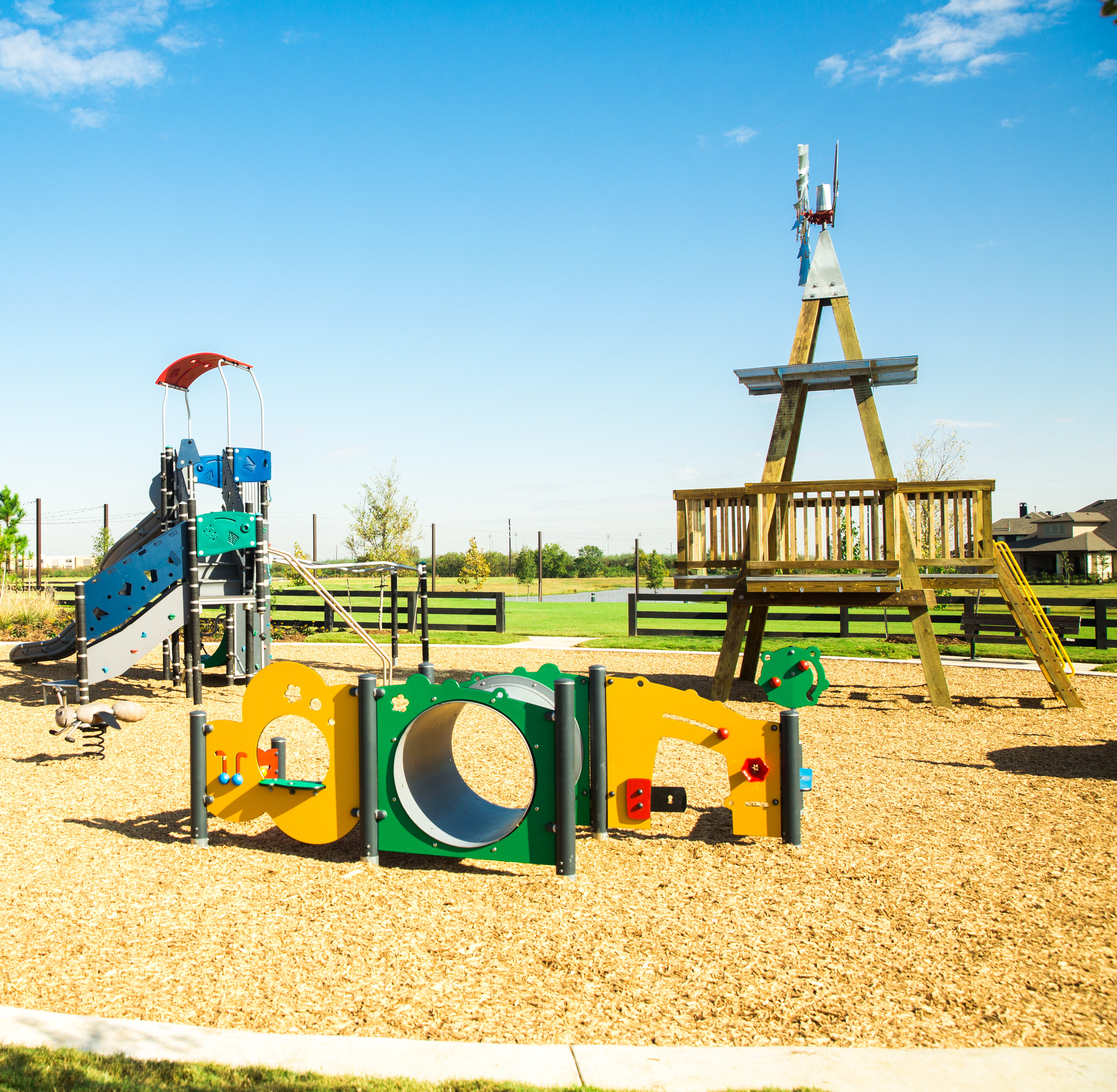 A colorful playground with various play structures, including a slide and climbing equipment, set against a backdrop of a clear blue sky and lush greenery.