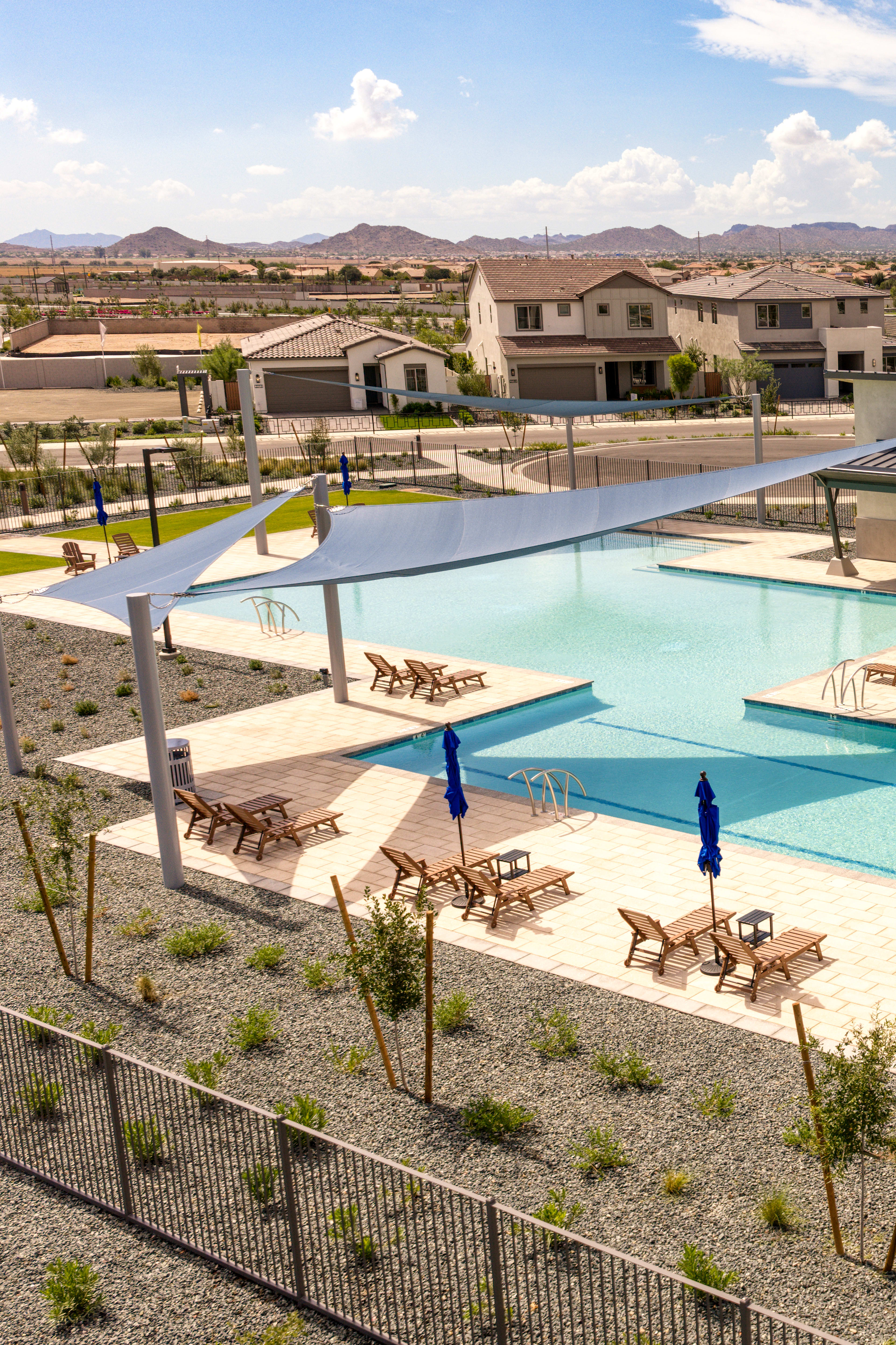 A residential community with a large swimming pool surrounded by buildings, chairs, and a mountainous landscape in the background.