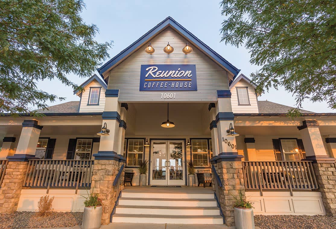 A cozy, rustic-style coffee house with a prominent sign reading "Reunion Coffee House" stands amidst a lush, green landscape with towering trees in the background.