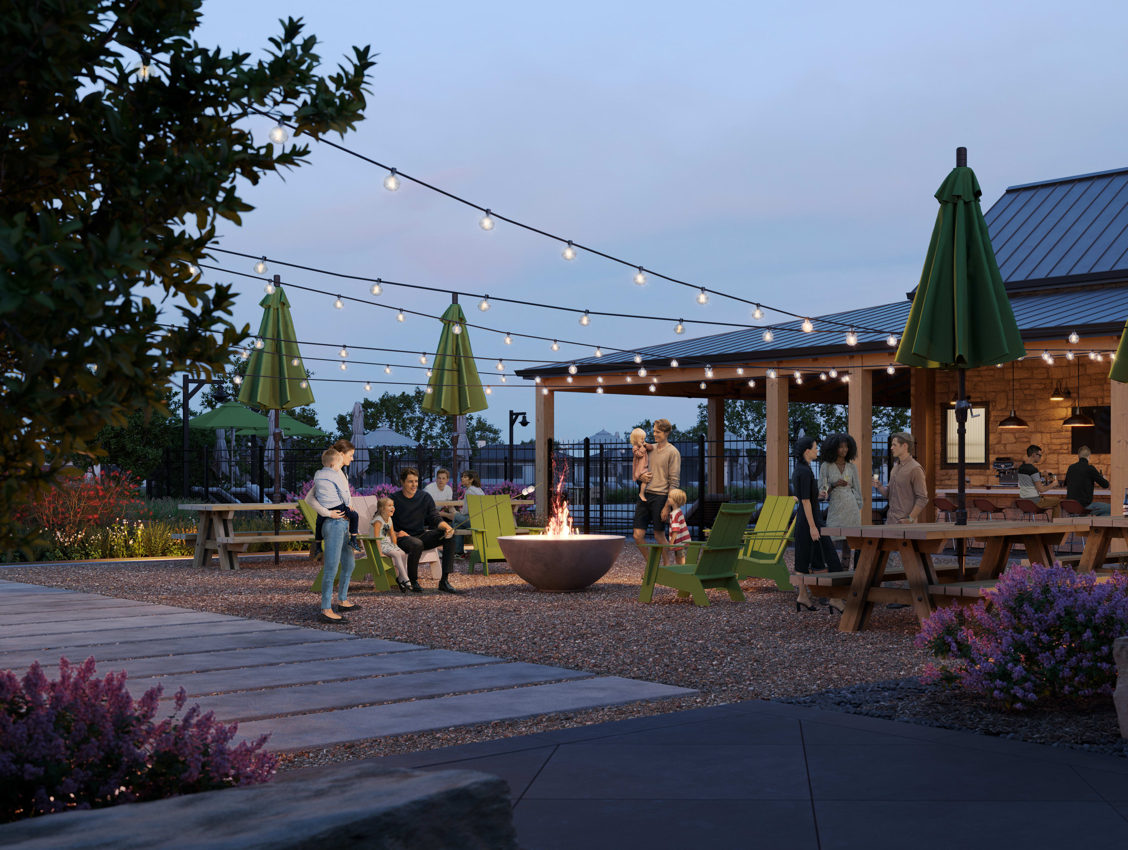 An outdoor dining area with string lights, umbrellas, and people seated at tables, surrounded by landscaping and a brick building in the background.