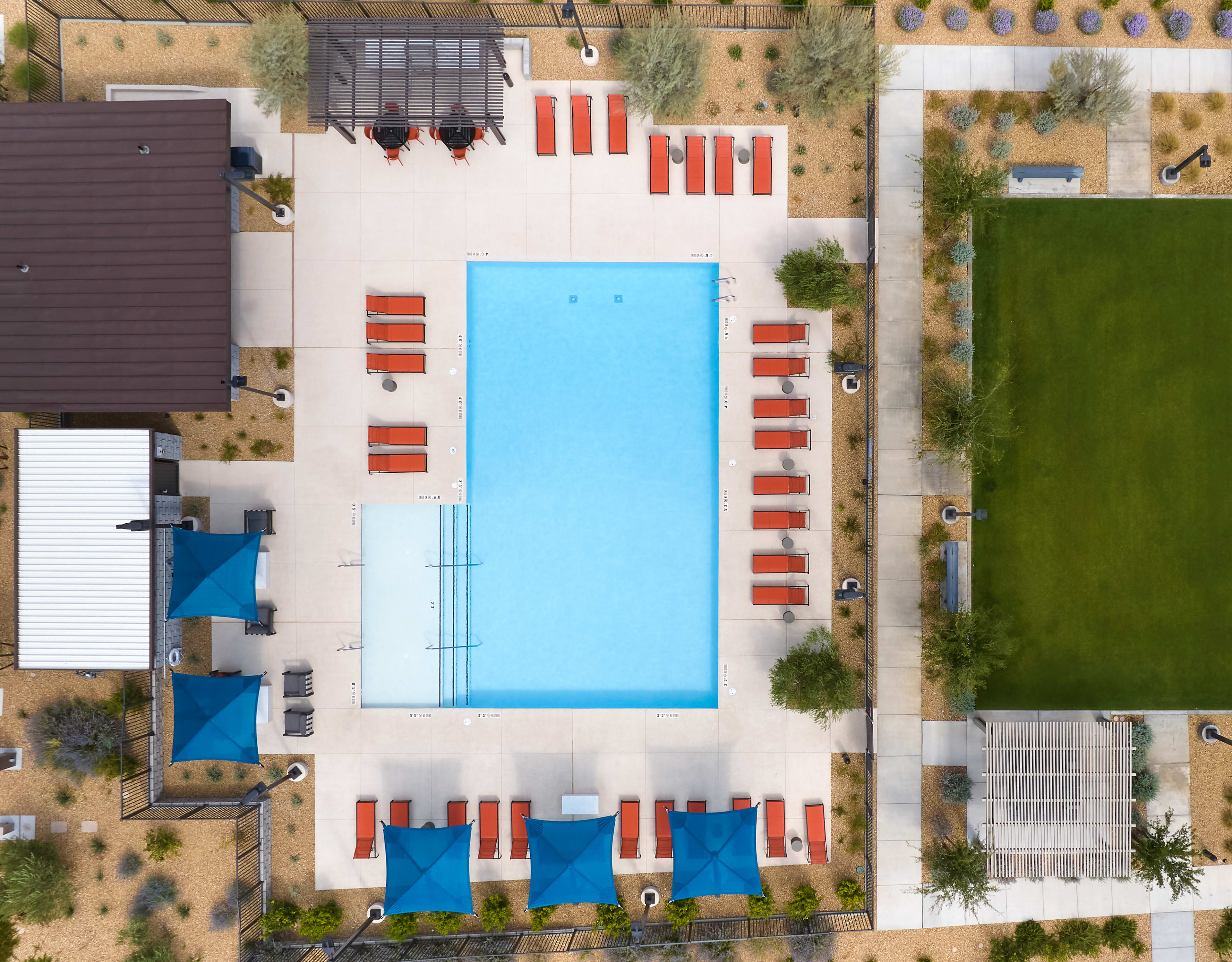 A modern, minimalist building with a large swimming pool surrounded by a grassy area and various architectural elements in the background.