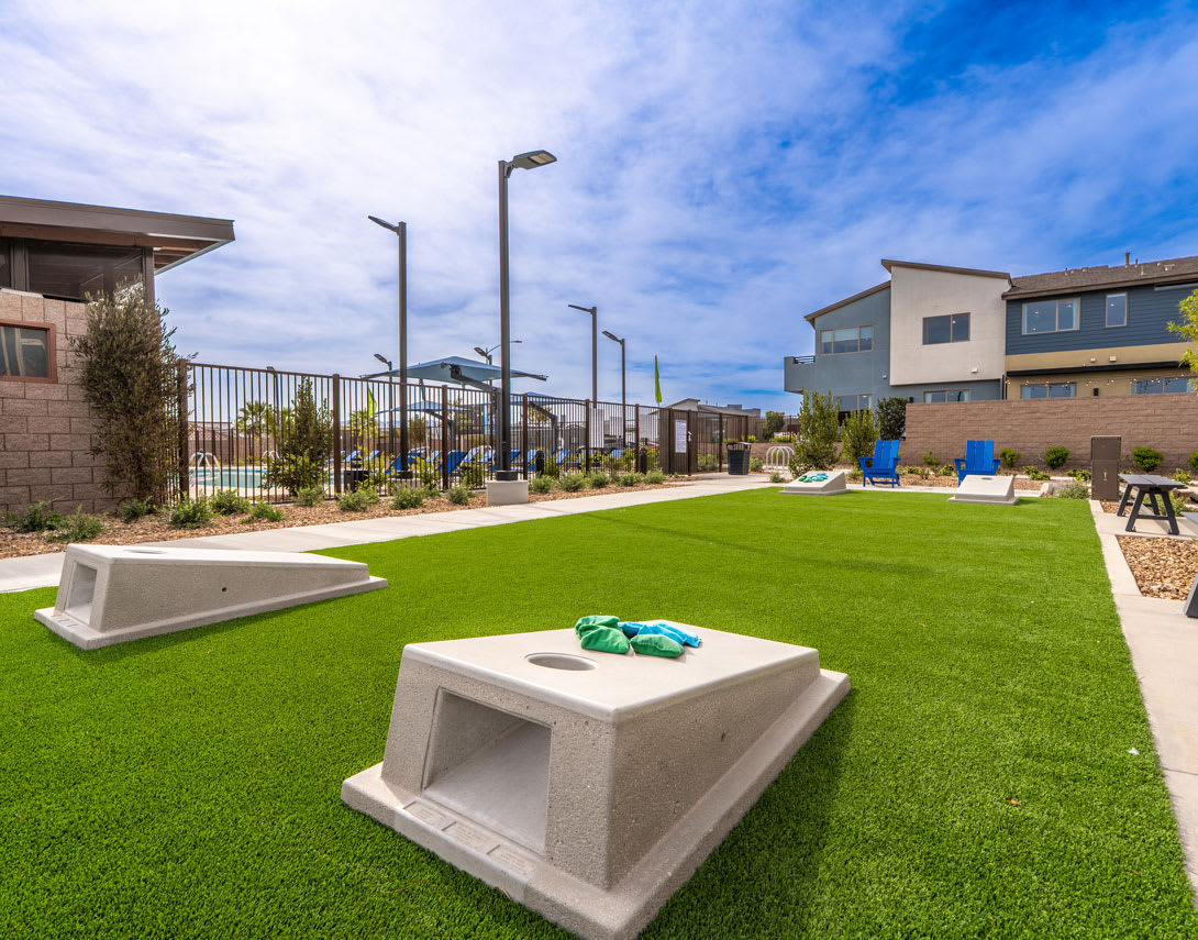 A well-manicured lawn with concrete benches sits in the foreground, surrounded by modern residential buildings and a clear blue sky in the background.