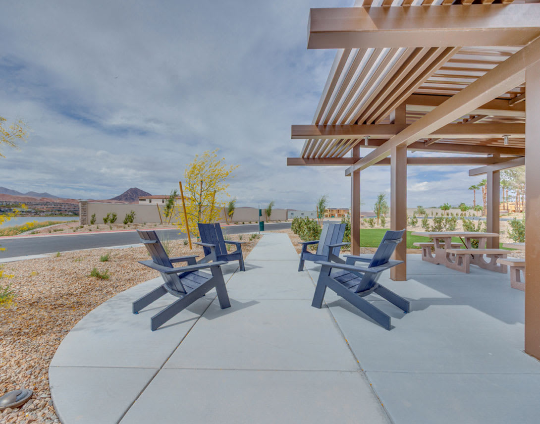 A wooden pergola structure with Adirondack chairs on a concrete patio, overlooking a scenic landscape with mountains in the background.