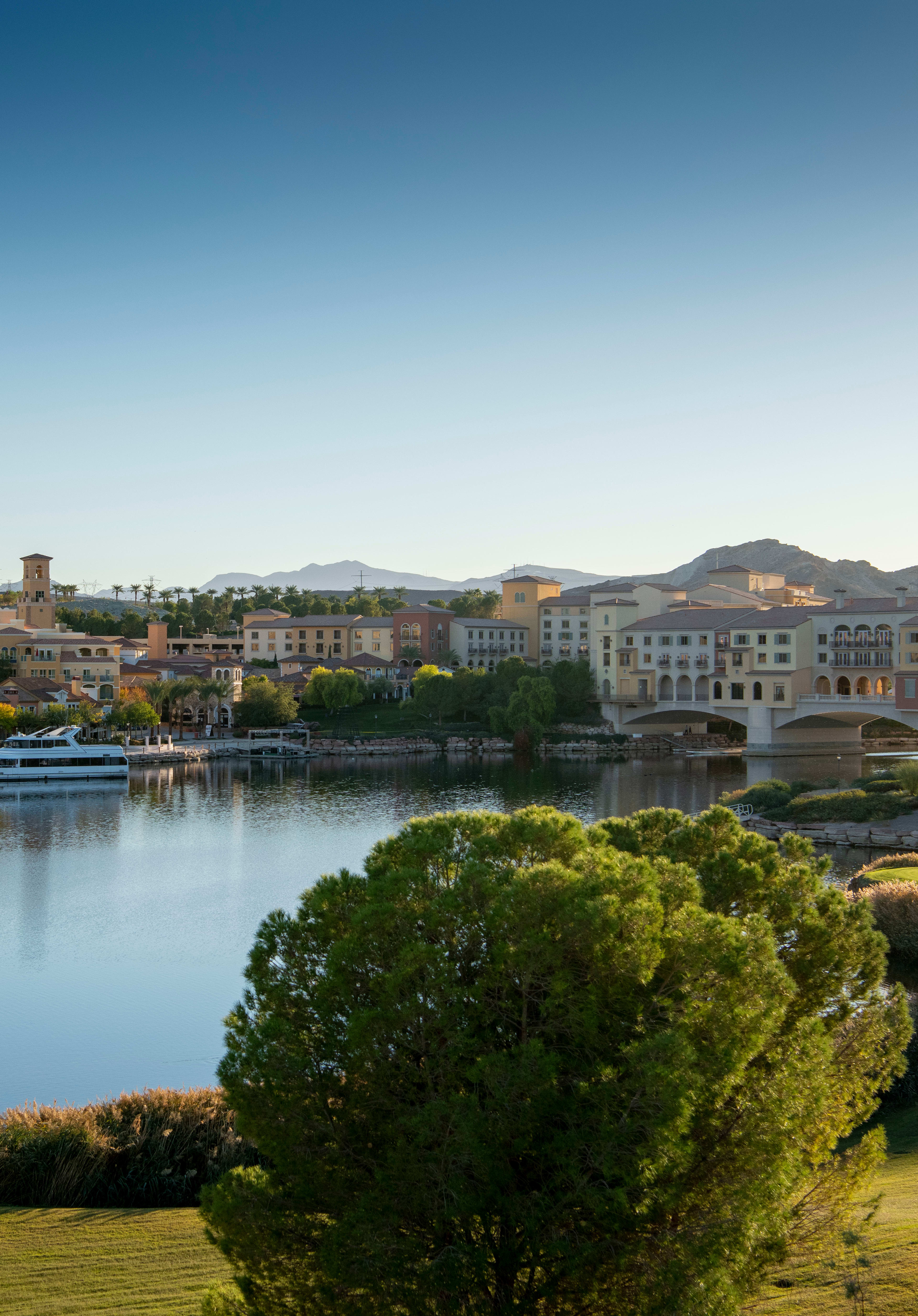 A picturesque town nestled along a tranquil lake, surrounded by lush greenery and towering mountains in the distance, creating a serene and idyllic landscape.