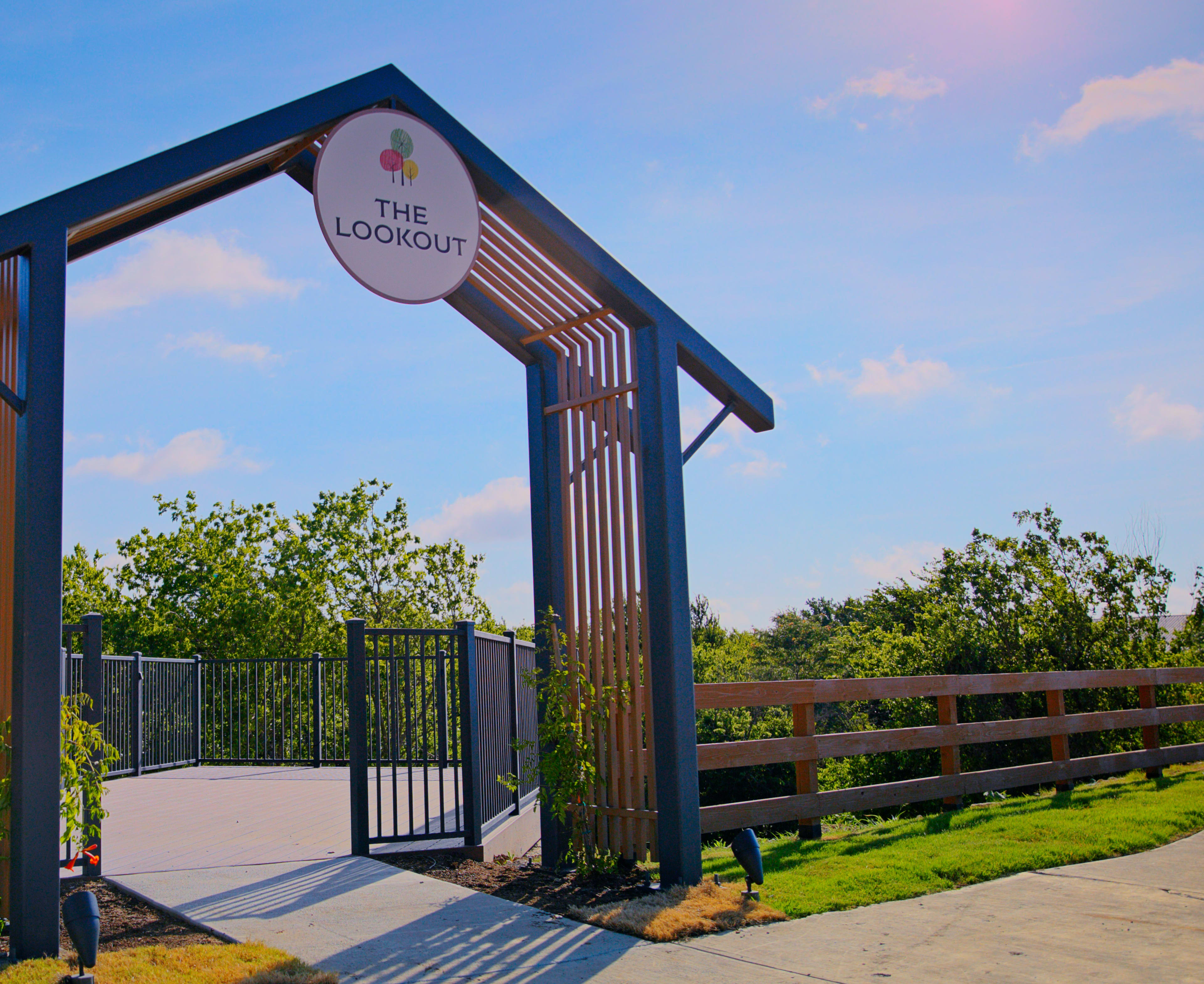 A large metal archway with the text "The Loop" stands in the foreground, surrounded by lush greenery and a paved walkway in the background.