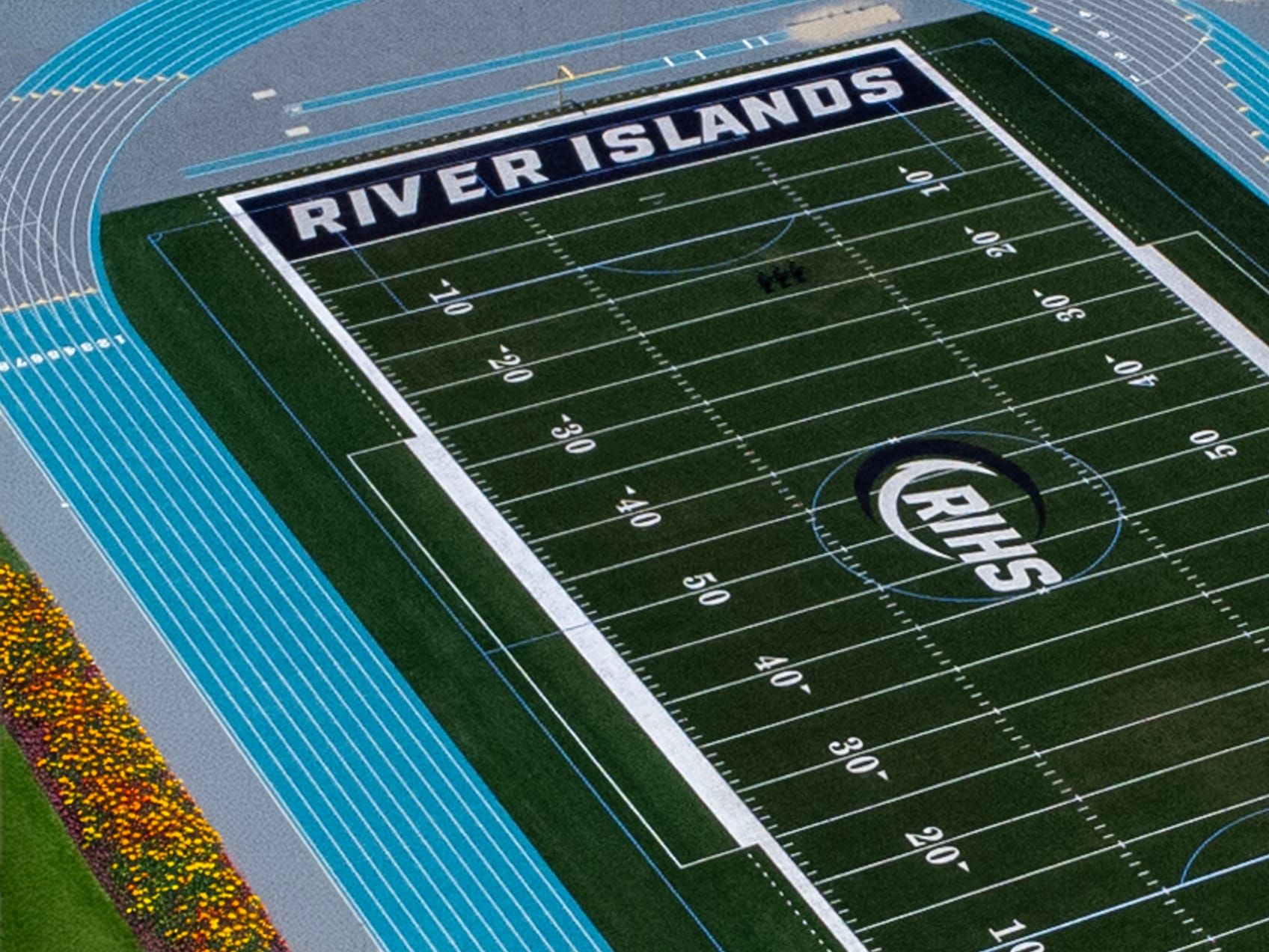 The image shows a football field with the text "RIVER ISLANDS" displayed prominently on the field. The background appears to be a stadium or sports facility, with blue and white striped structures visible.