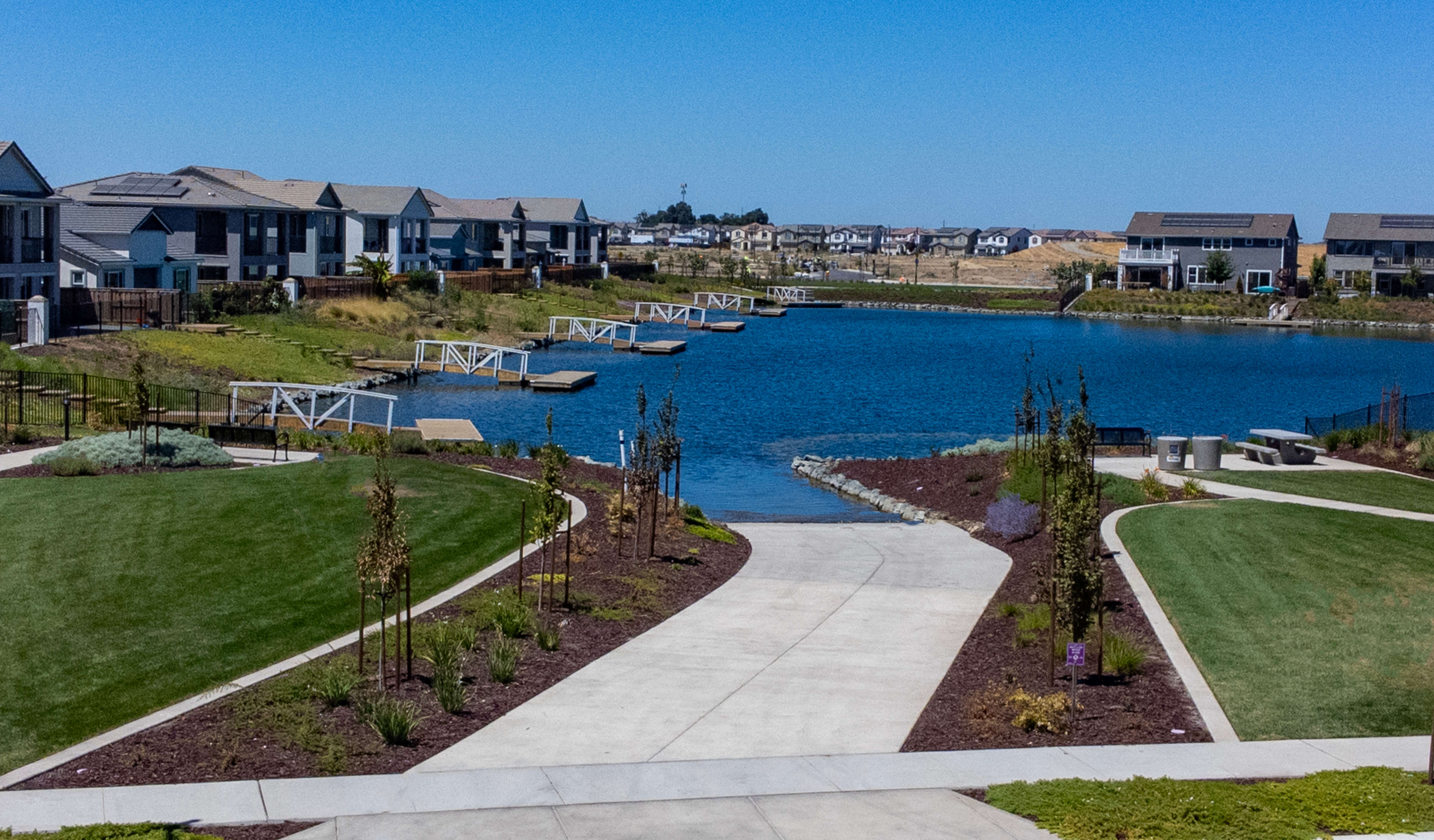 A well-manicured walkway leads through a lush, landscaped community with a picturesque lake and surrounding residential buildings in the background.